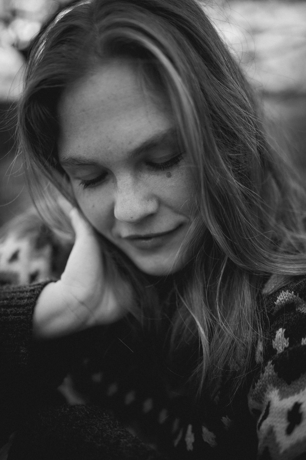 Black and white portrait of a person with long hair smiling with eyes closed in a patterned sweater.