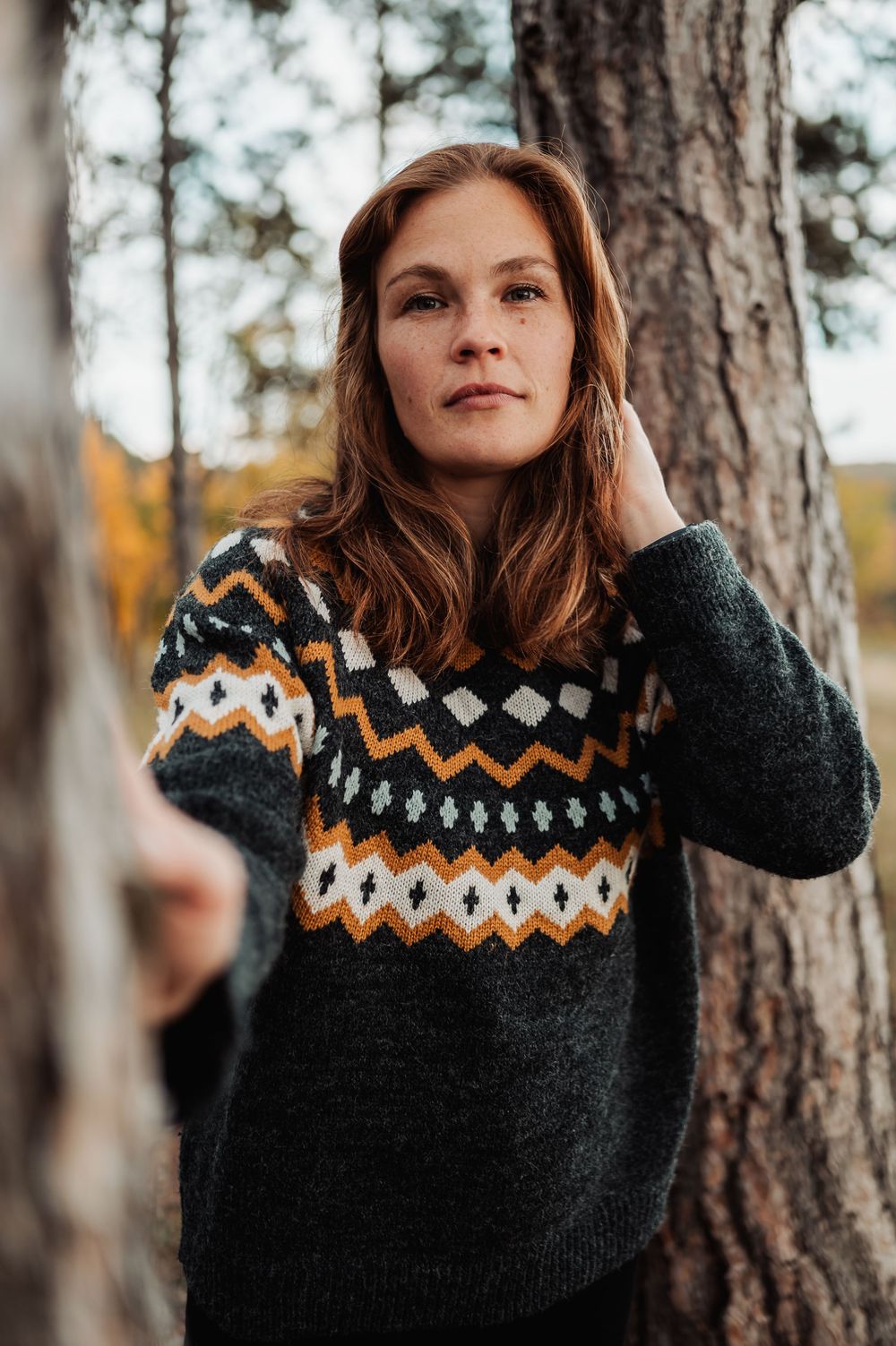 Person in dark Nordic-style sweater with zigzag pattern poses in forest setting.