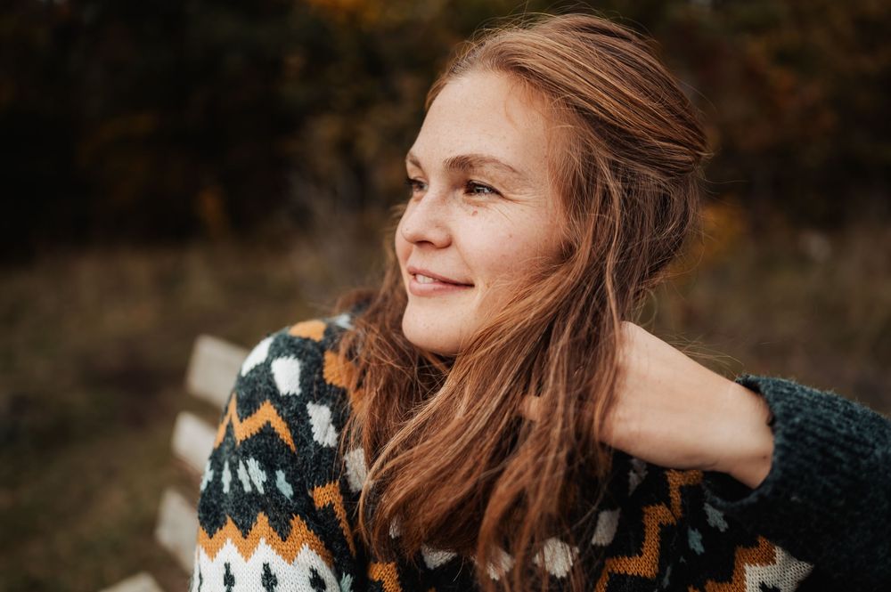 A person wearing a patterned knit sweater smiles while looking away in warm autumn lighting.