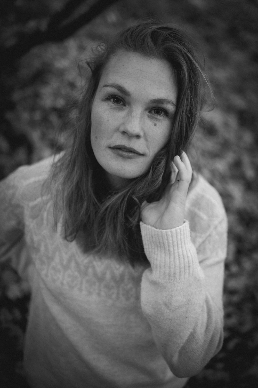 Artistic black and white portrait of a person in a cozy sweater with natural lighting and soft expression.