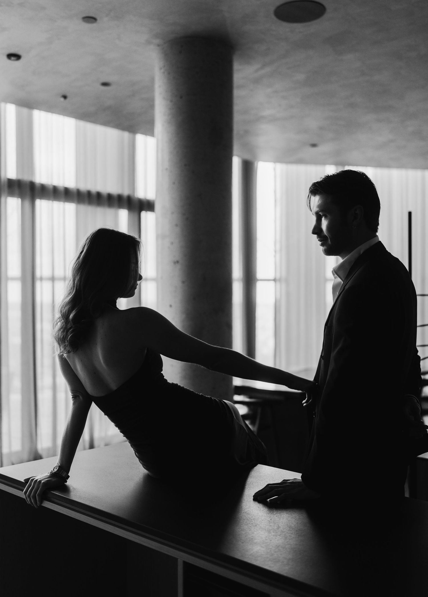A dramatic black and white silhouette of a couple in an elegant interior with large windows and a modern column.