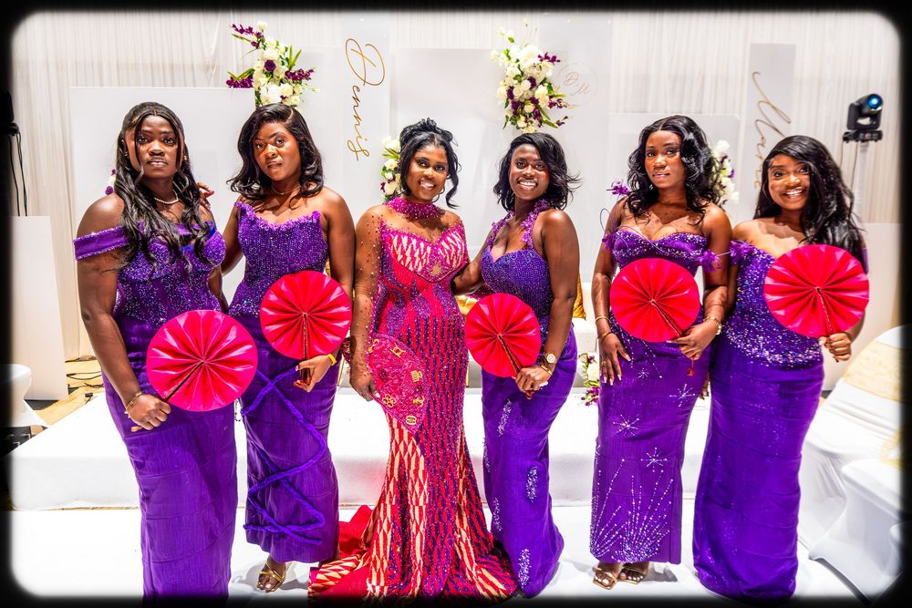 Wedding party in purple dresses poses with bright red and pink paper fans during celebration.