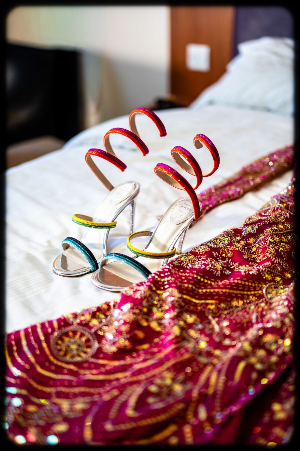 White strappy sandals rest on a shimmering pink and gold sequined fabric creating an elegant bridal detail shot.