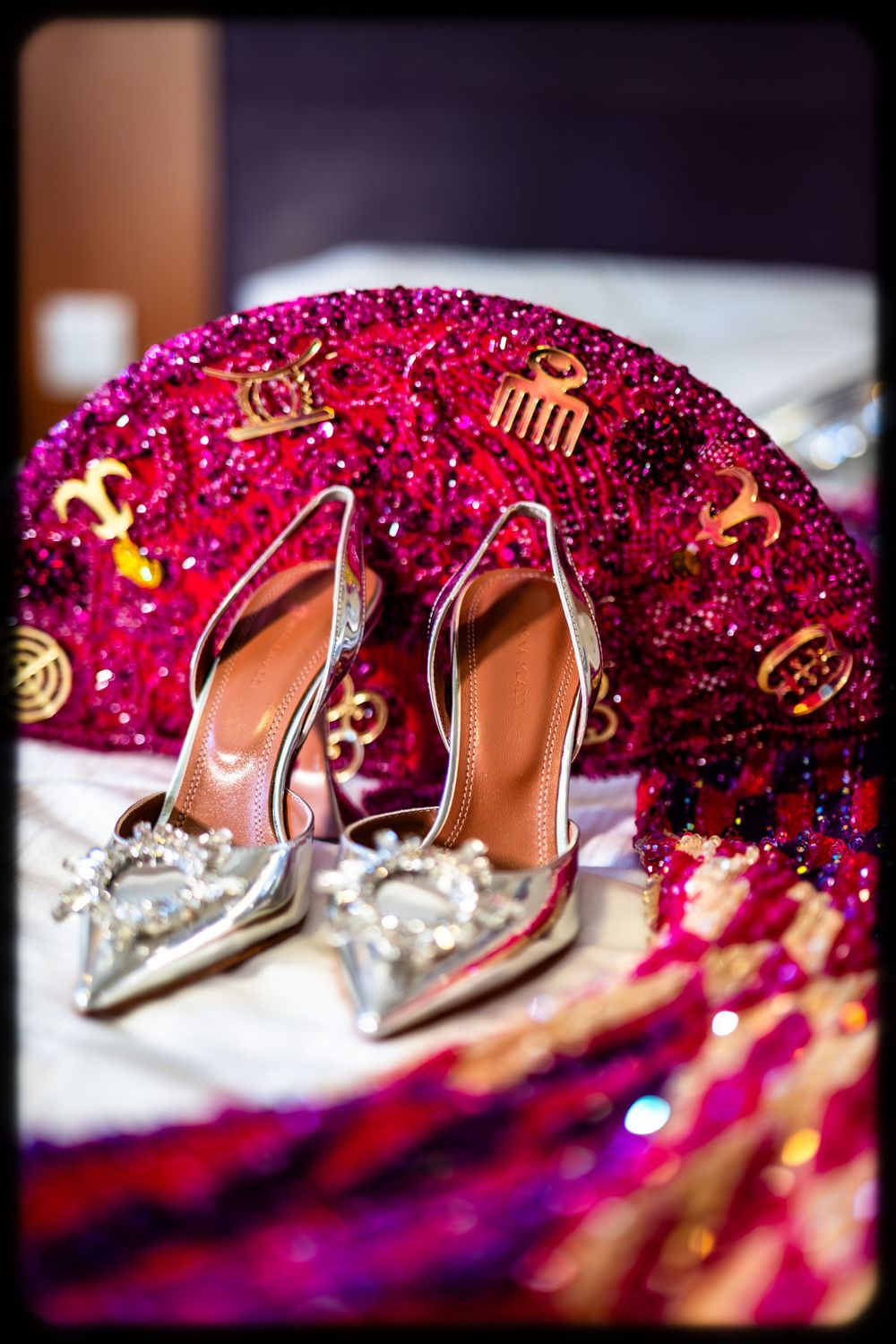Elegant silver crystal-embellished bridal shoes displayed against a vibrant pink sequined Indian wedding lehenga background.
