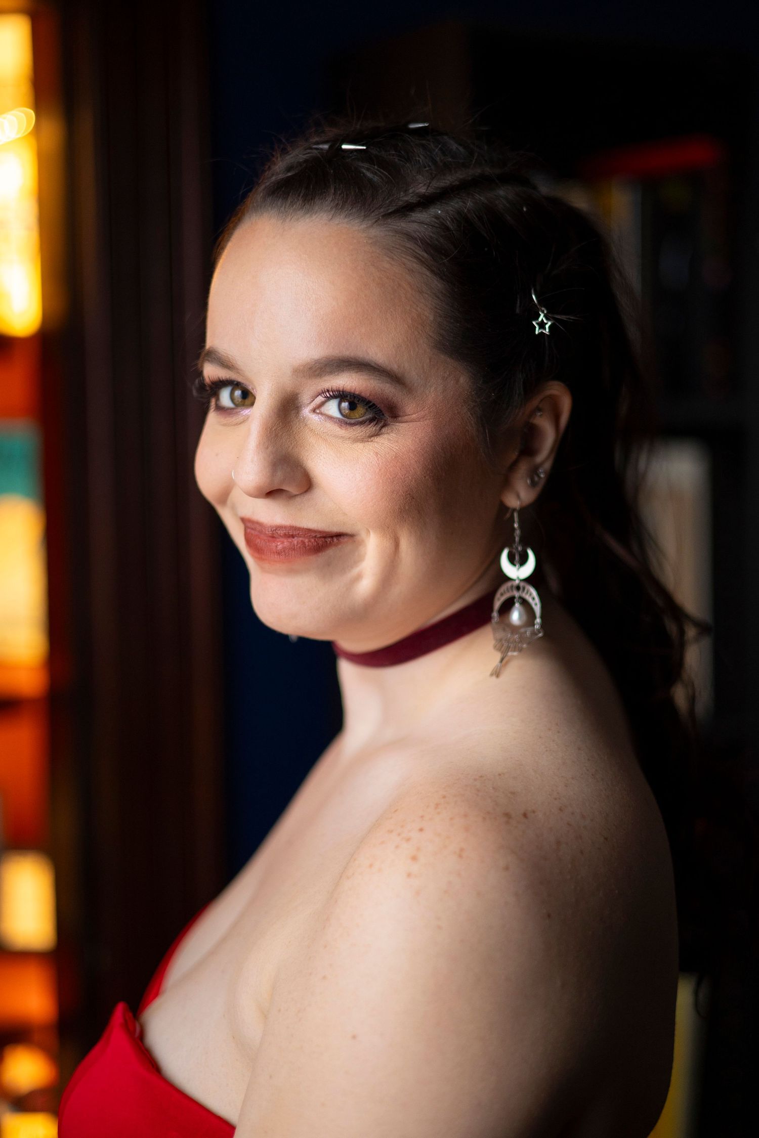 Portrait of a woman in a red gown and velvet choker smiling over her shoulder with crescent moon earrings on her wedding day.