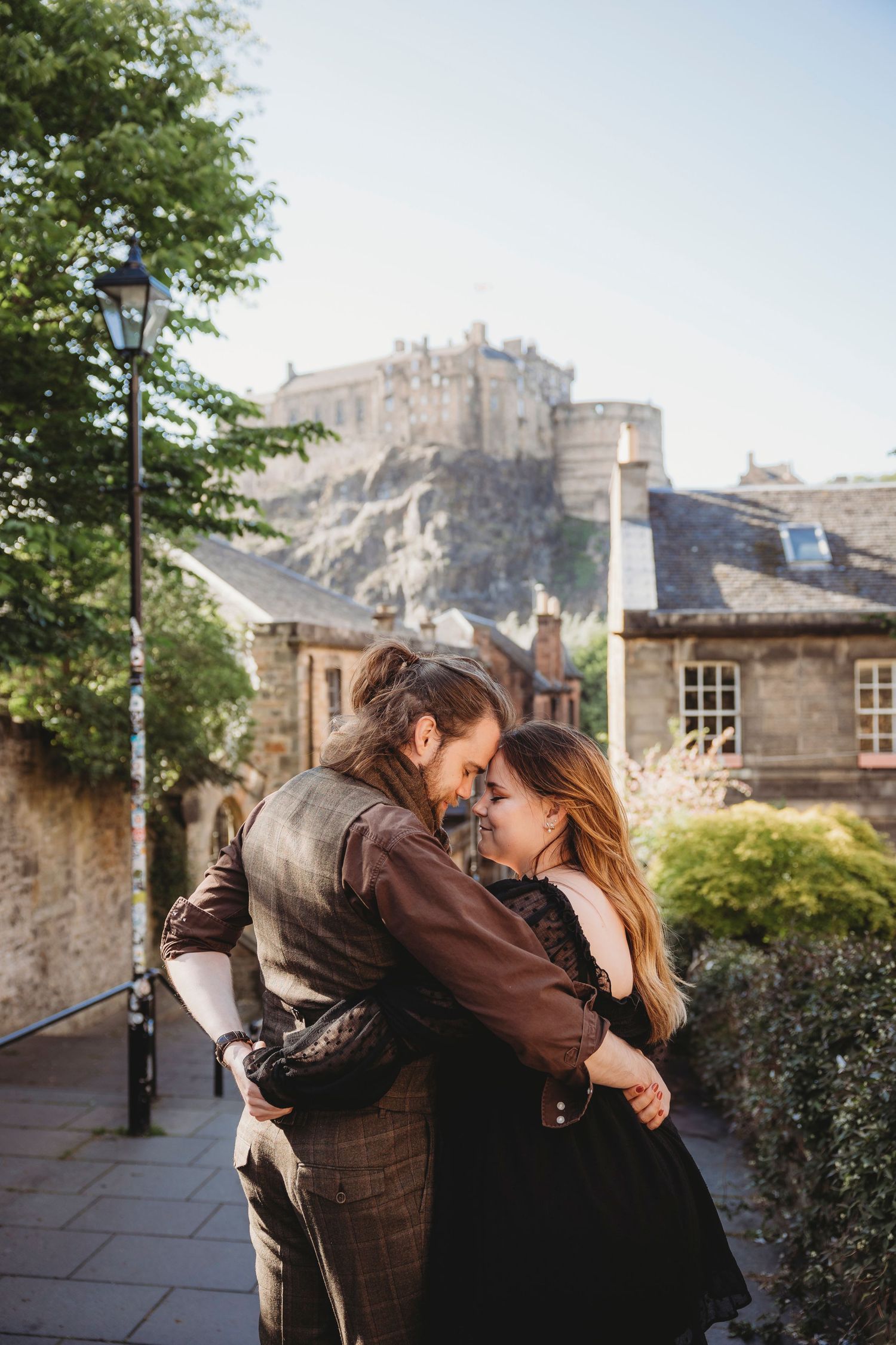 A romantic couple embraces in front of Edinburgh Castle on a sunny day in Scotland.