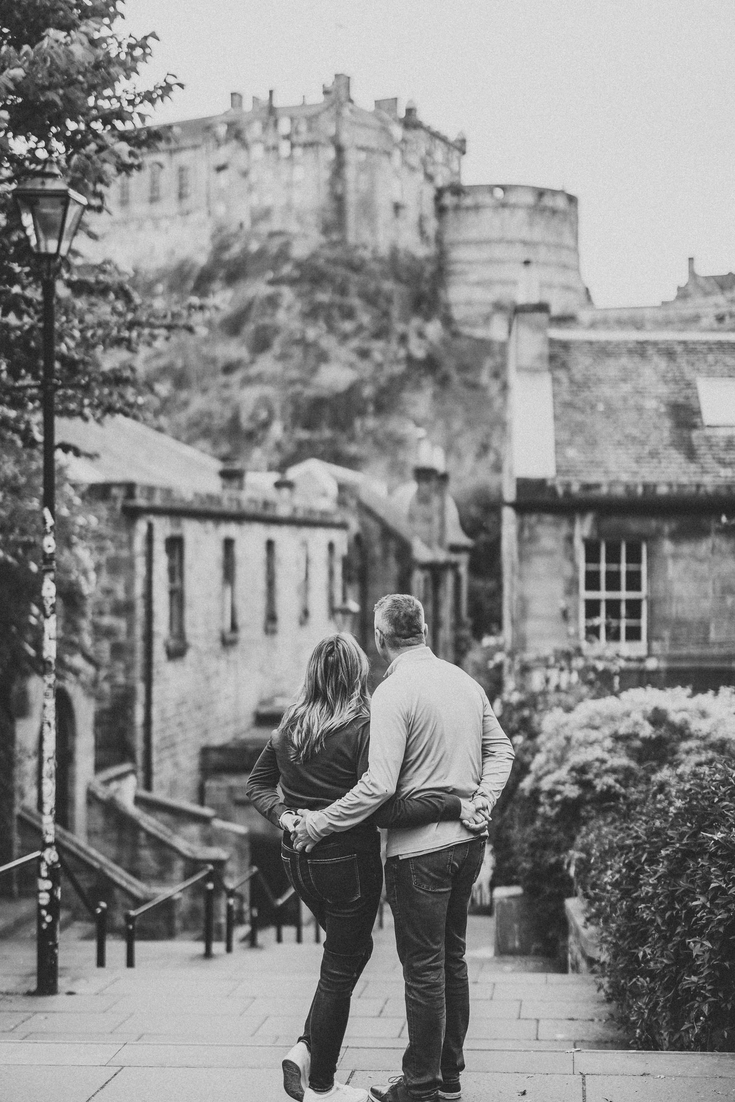 A couple walking along a scenic cobblestone street in Edinburgh with the historic castle visible in the background.