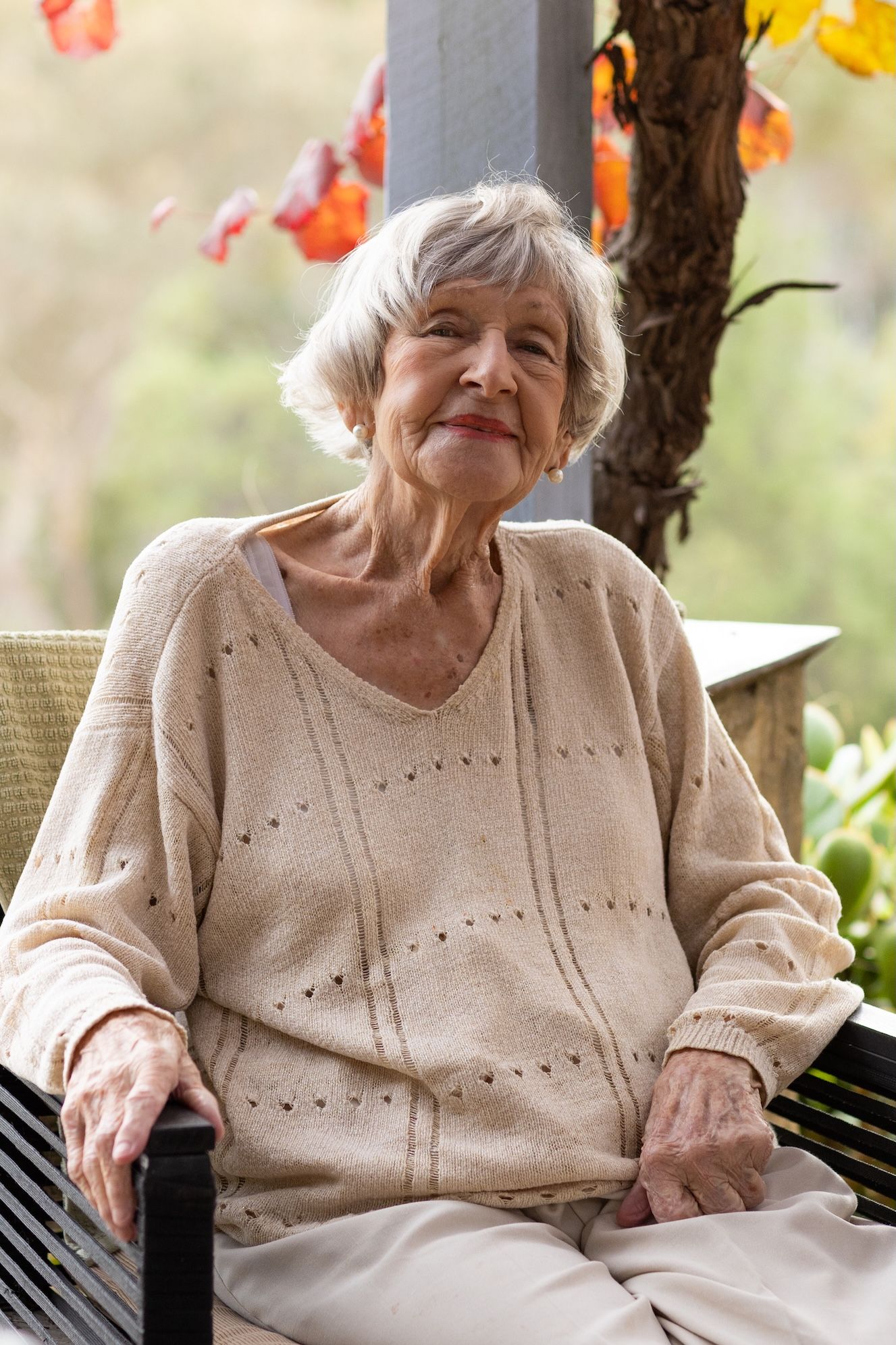 An elderly person in a beige sweater sits outdoors smiling warmly in a series of candid portrait shots.
