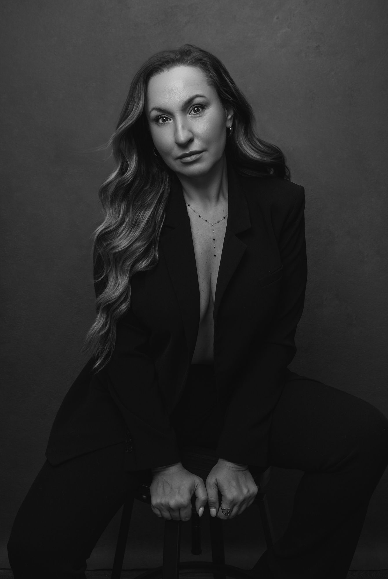 A black and white portrait series showing a woman in a dark blazer posing against a dramatic shadowy background.