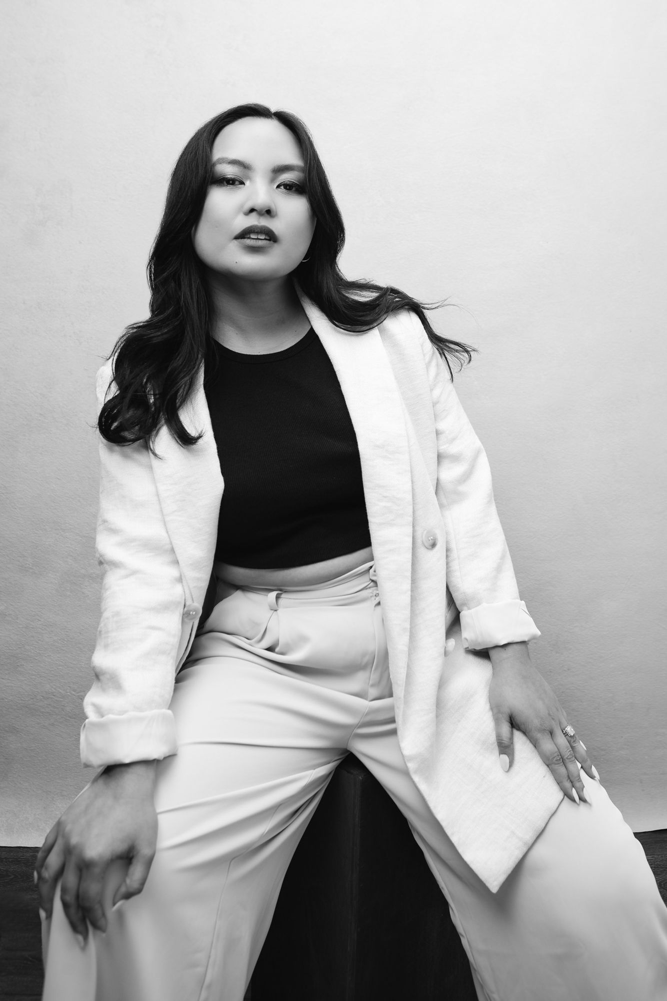 A black and white photo series showing a figure in a white blazer and black top posing against a light background.