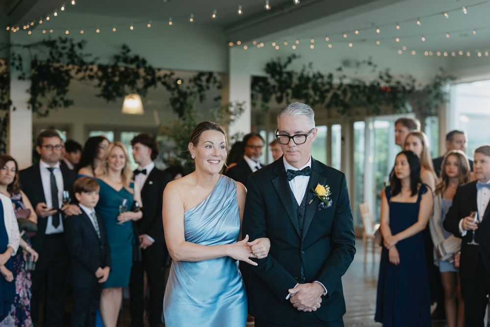 Wedding guests dance and celebrate during an evening reception under string lights in an elegant indoor venue.