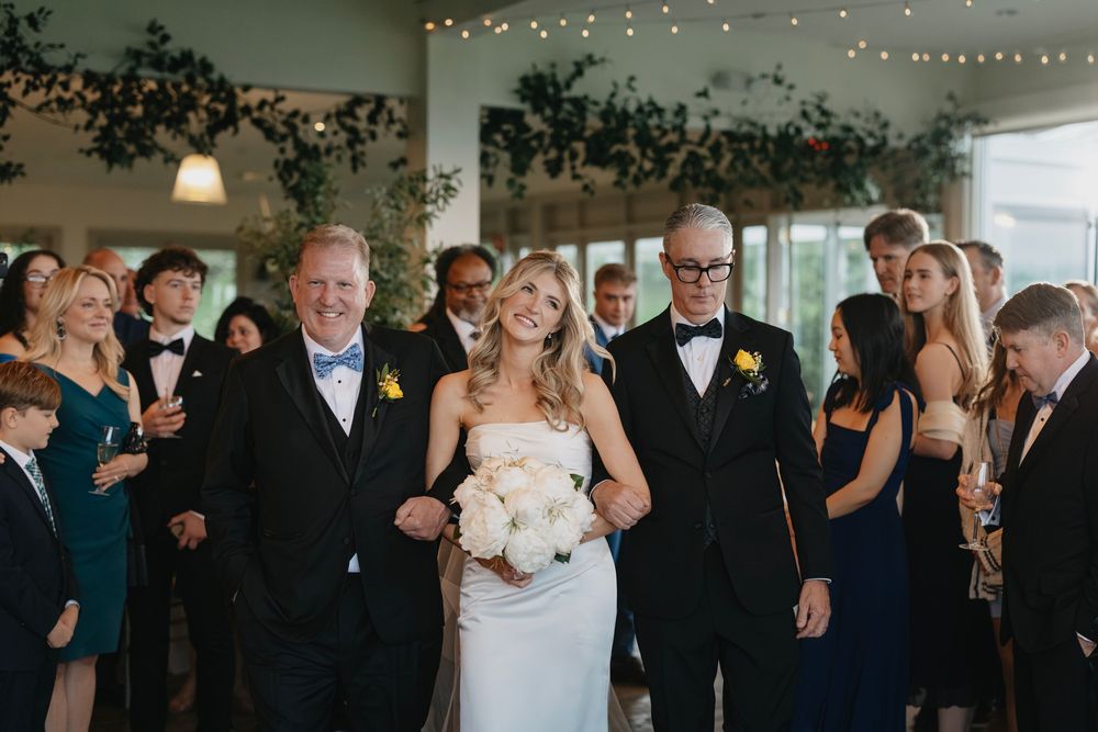 A wedding reception celebration with guests dancing and mingling under decorative string lights and greenery.