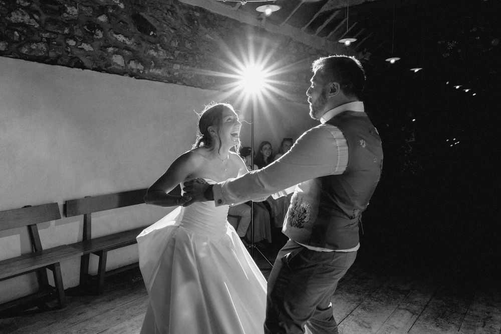 A couple dances together at their wedding reception with a bright light flare in black and white photography.