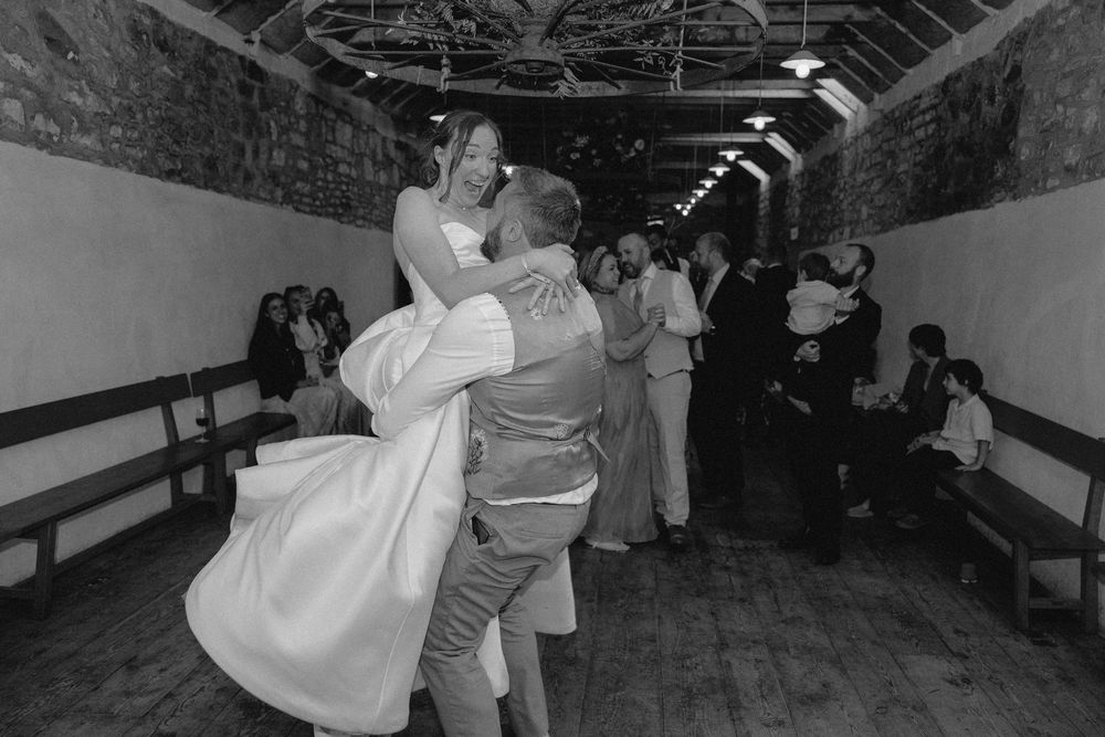 A couple dances together in a rustic hallway during a wedding celebration while other guests look on.