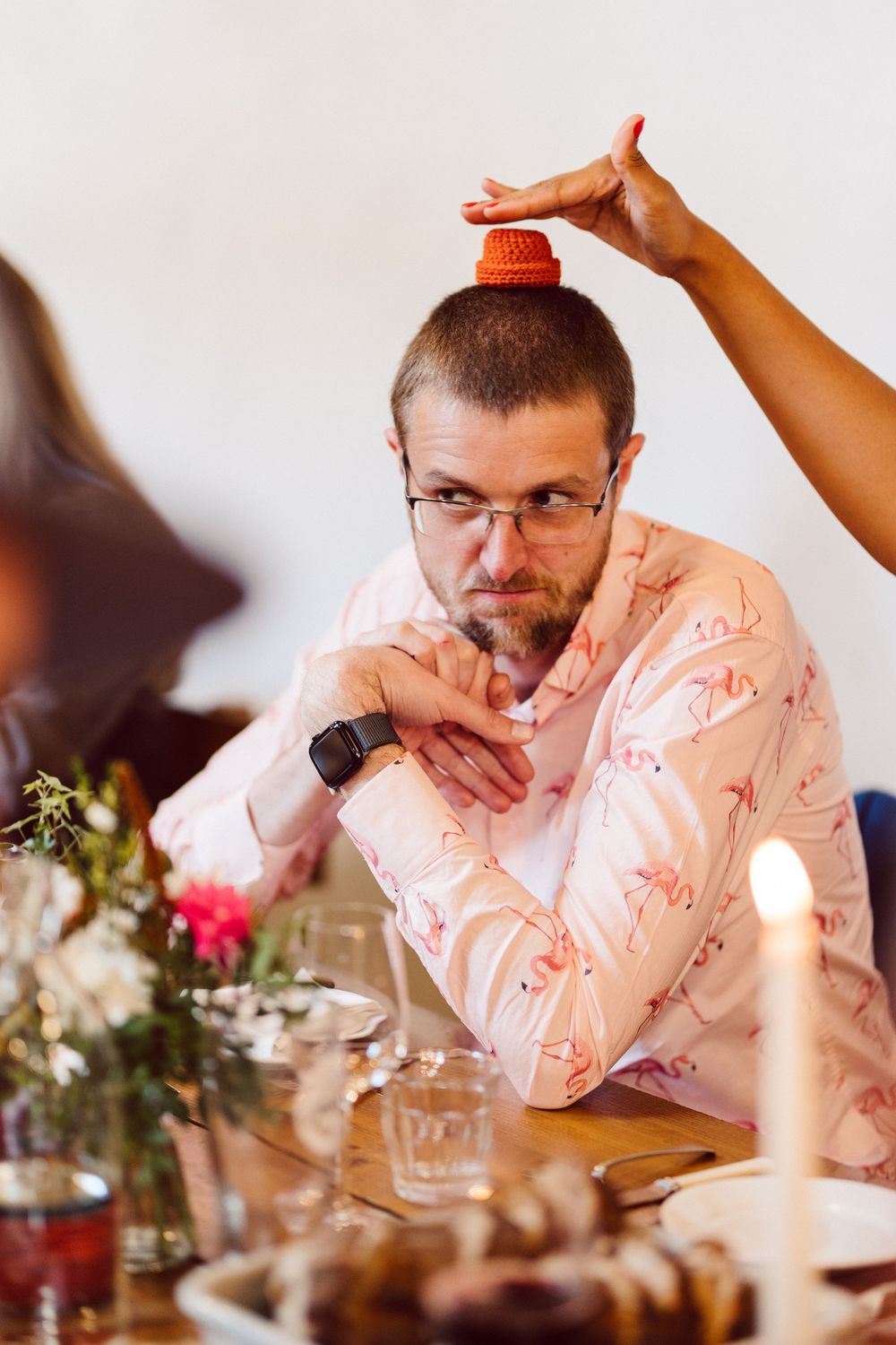 A guest at a wedding reception laughs while wearing a pink patterned shirt at a decorated dining table.