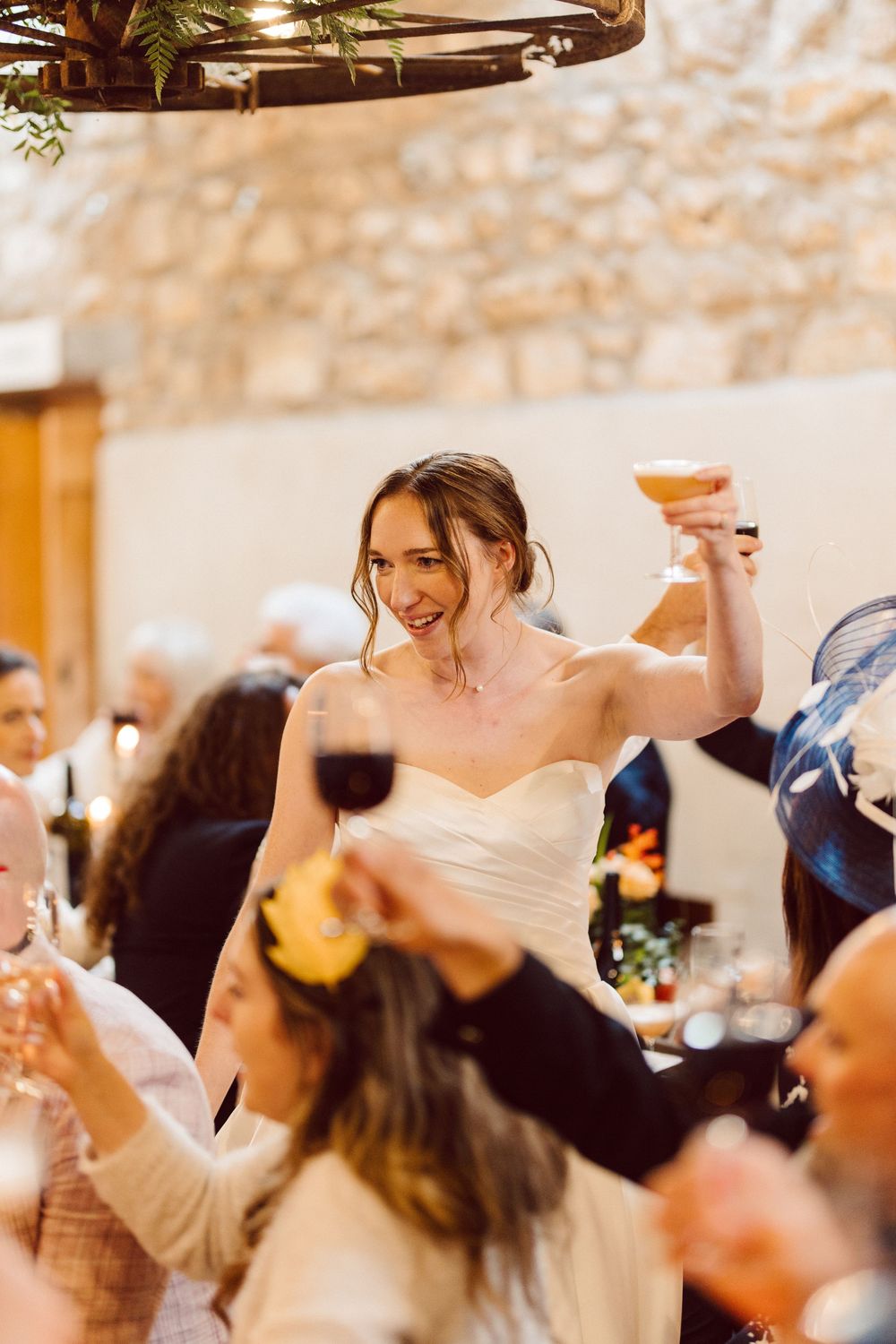 Wedding guests raise their glasses in celebration during a joyful toast at an indoor reception.