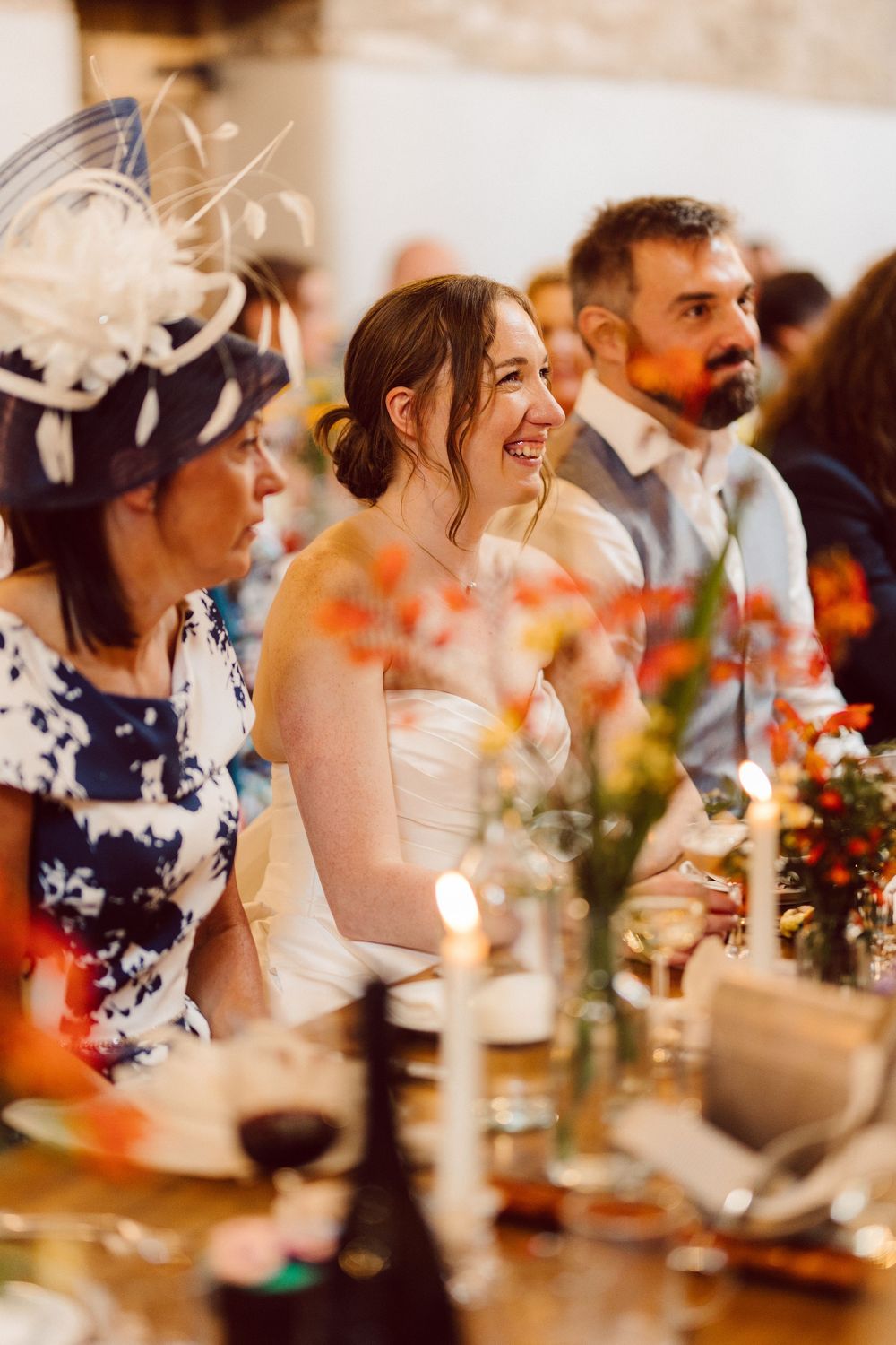 Wedding guests enjoy a candlelit reception dinner with floral centerpieces and warm lighting creating a joyful atmosphere.
