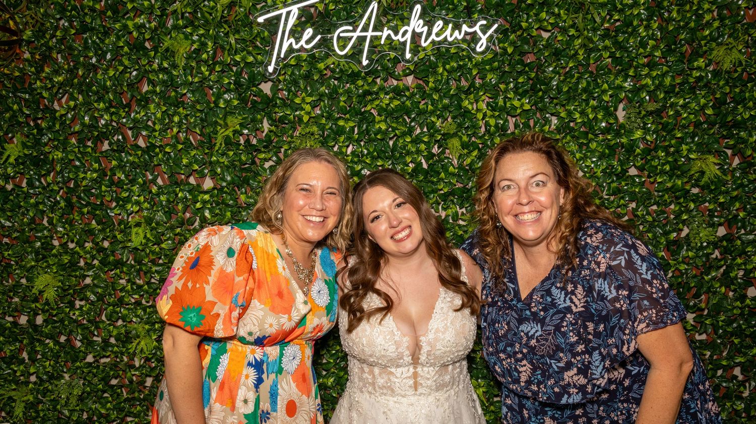 Guests mingle and celebrate at an outdoor garden party with lush green foliage wall backdrop.