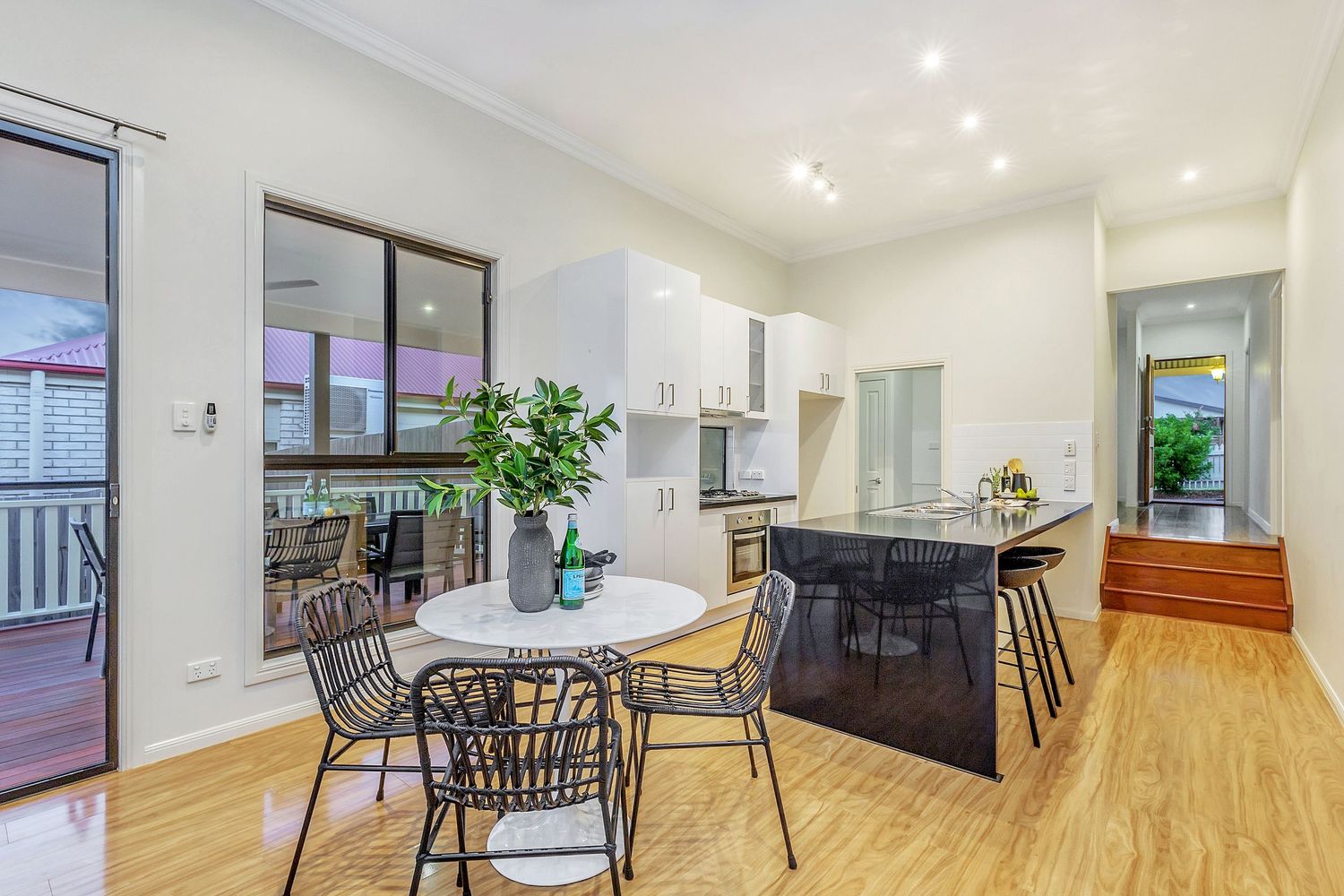 Modern open-plan kitchen and dining area with white cabinetry, black island bench, and timber flooring.