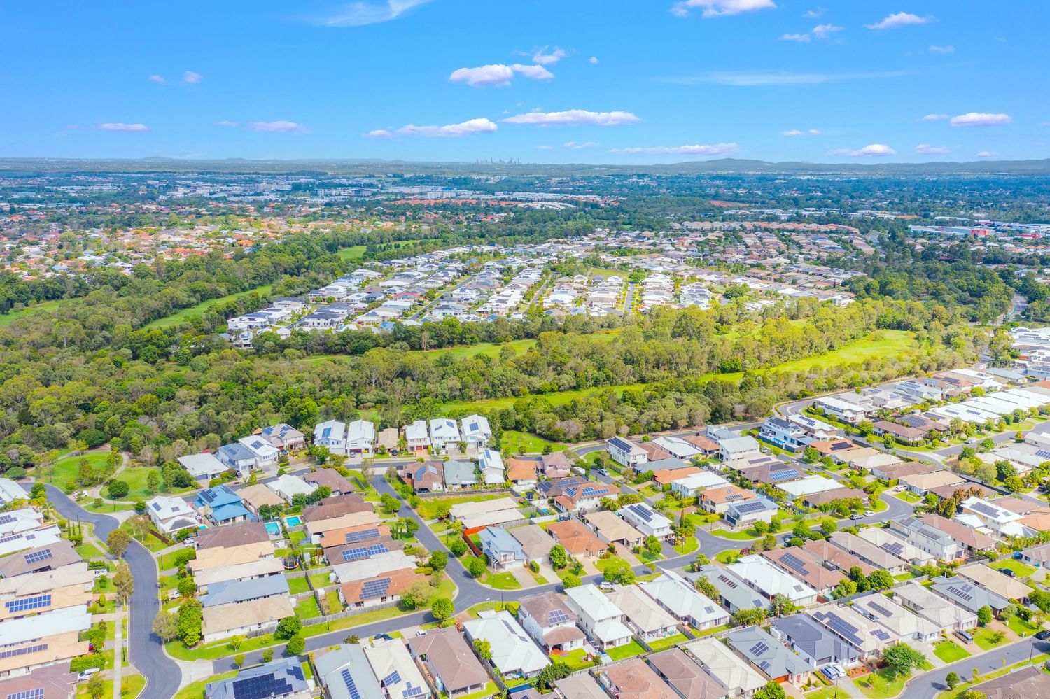 Aerial view of a suburban residential neighborhood with tree-lined streets and parklands under blue sky.