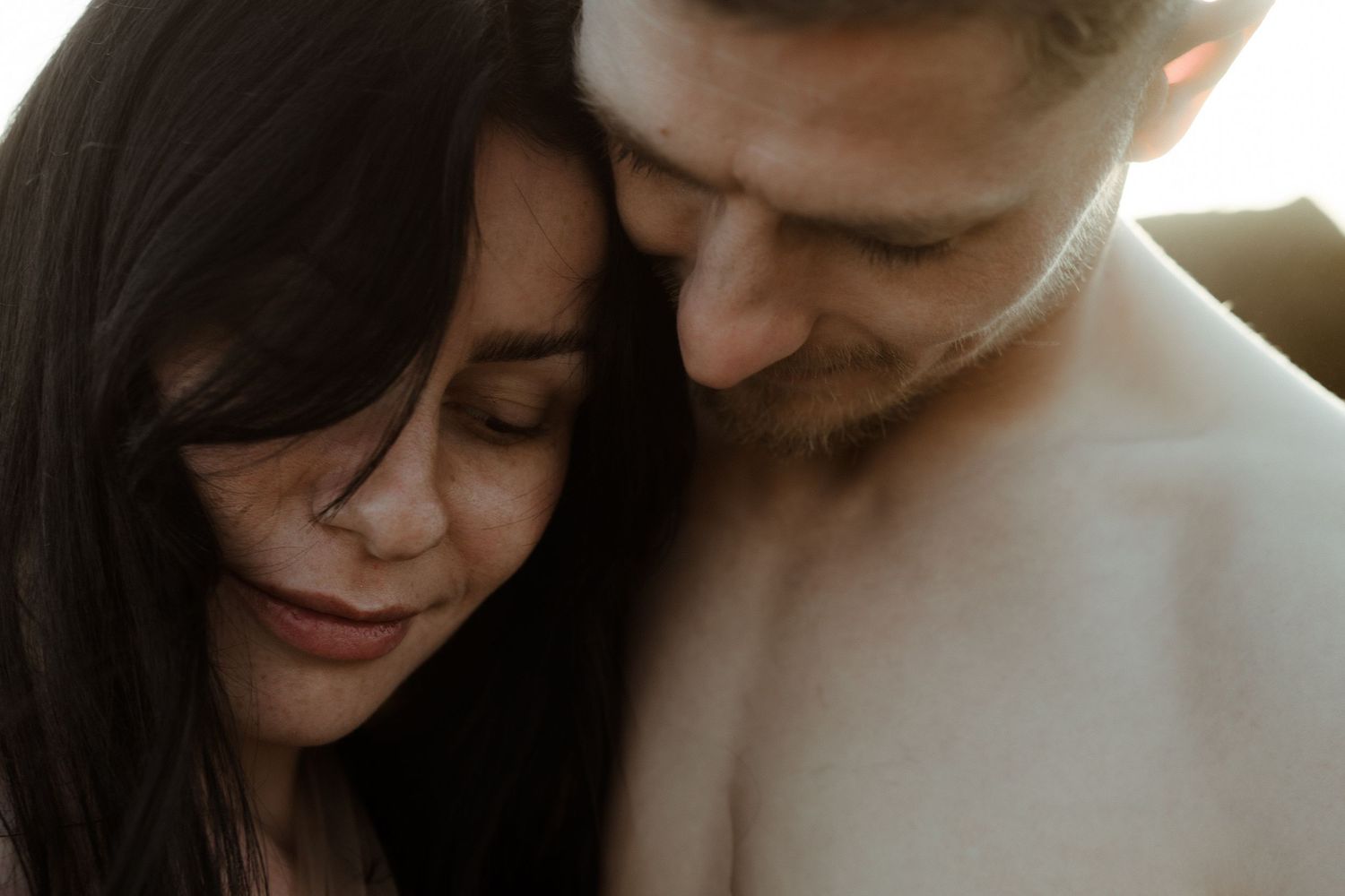 Intimate close-up portrait of a couple sharing a tender moment in warm lighting.