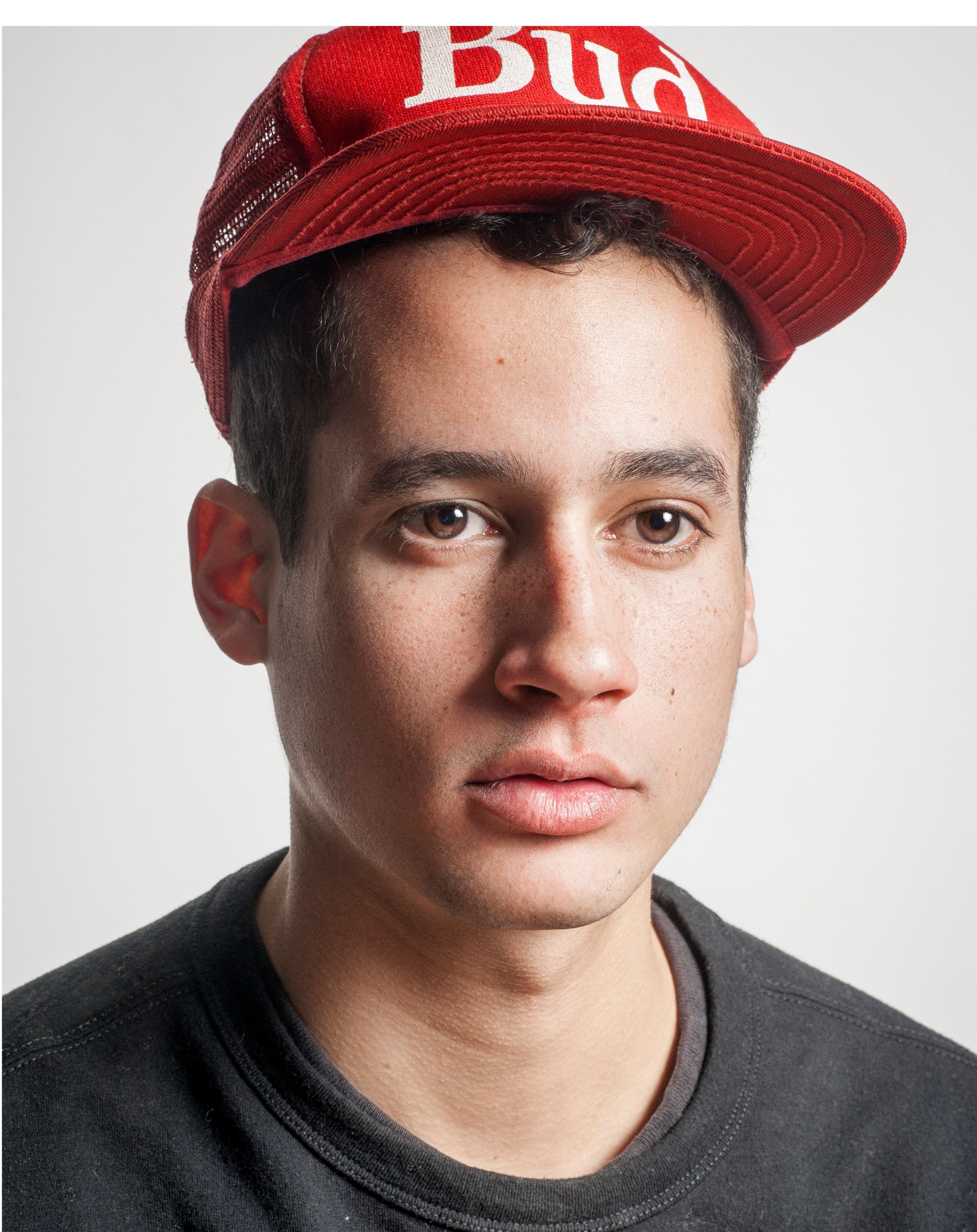 Young man wearing a red Budweiser snapback cap and black t-shirt posing for a portrait photo.