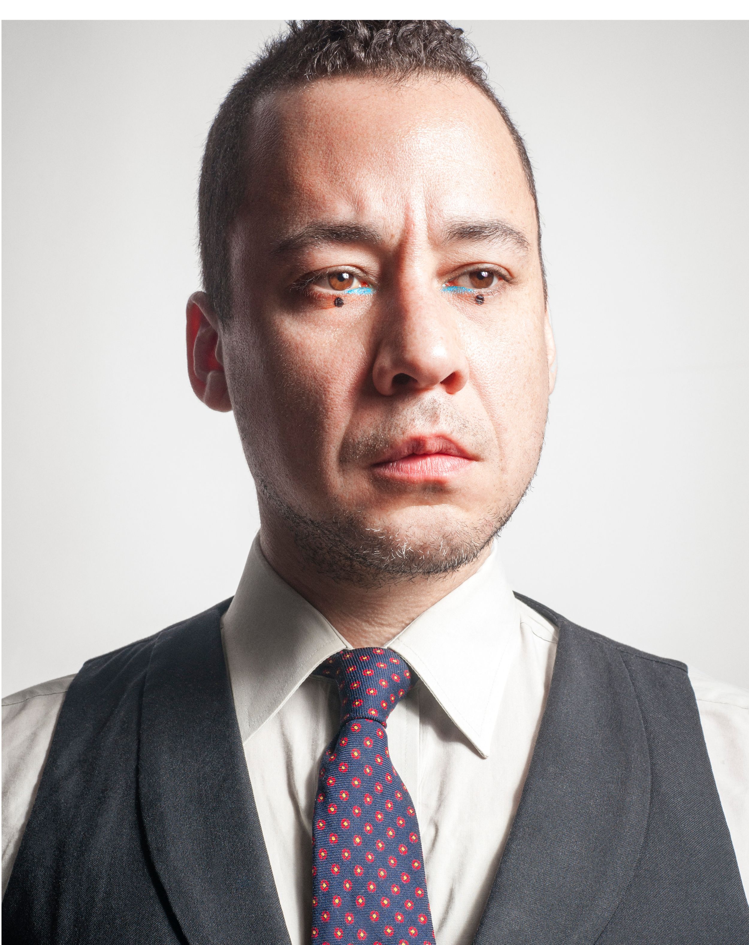Professional man in suit vest and polka dot tie posing for a formal portrait against gray background.