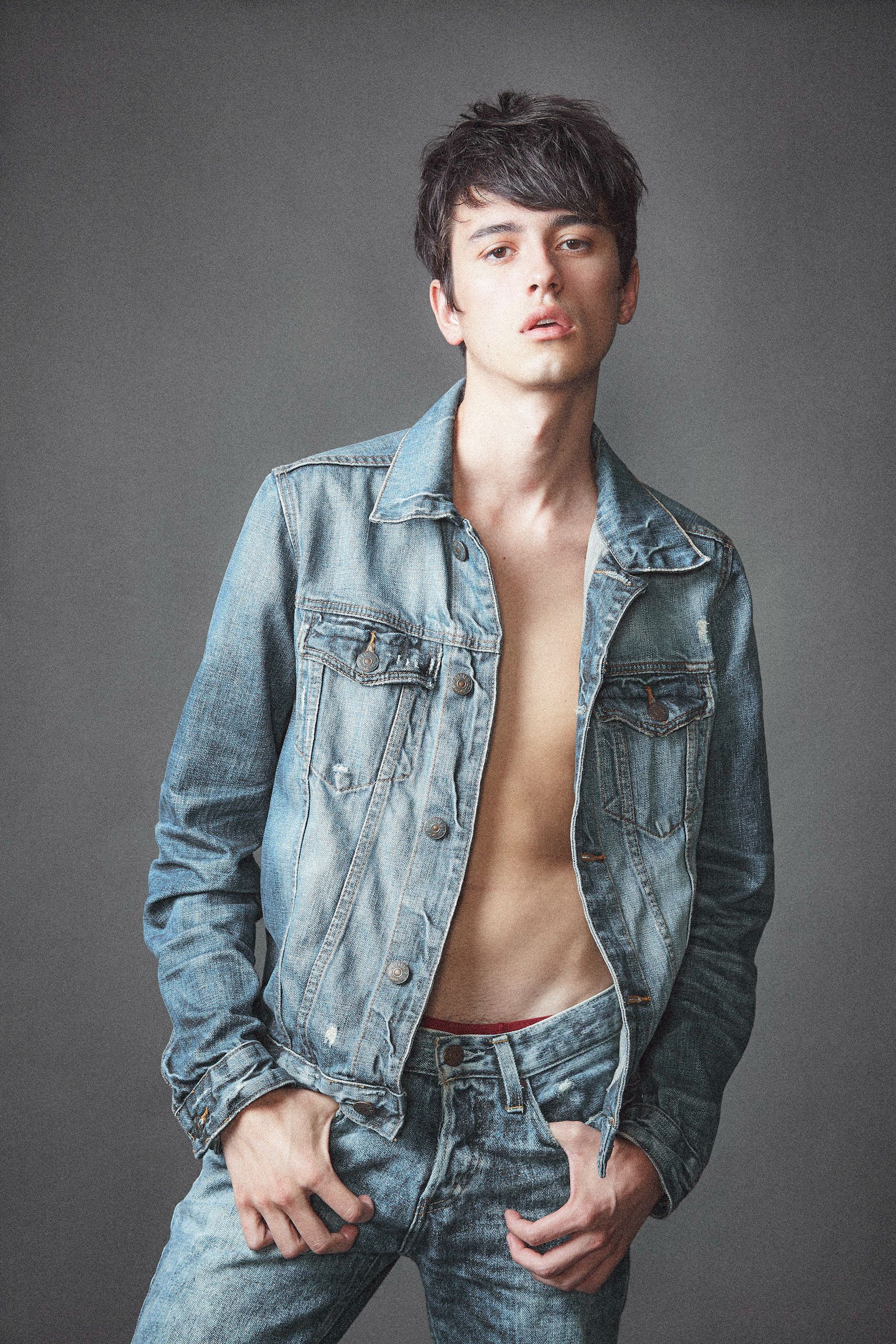 Model wearing light blue denim jacket in fashion photoshoot against gray background.