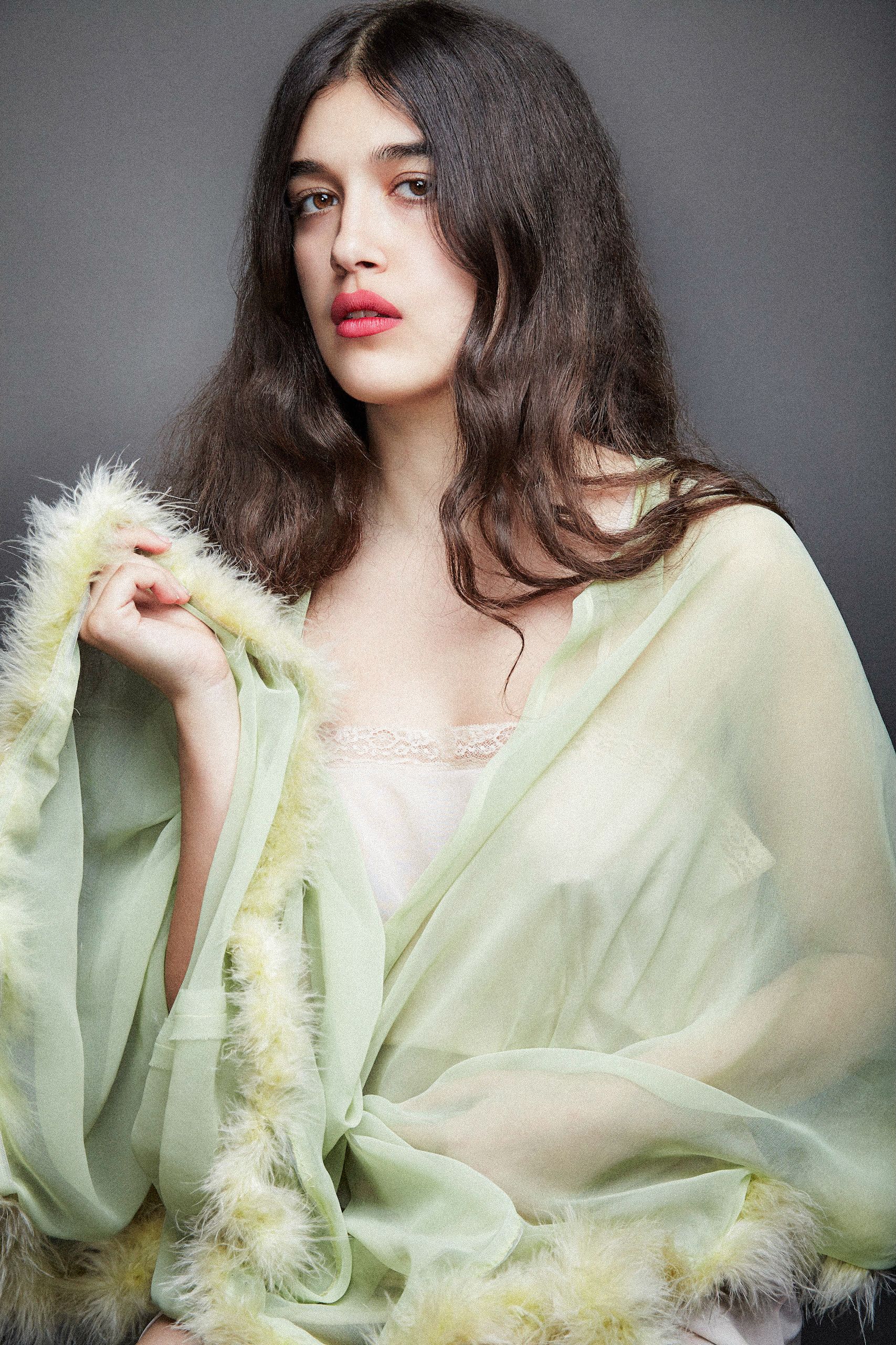 Fashion portrait in soft mint green sheer fabric with delicate feather trim details against a neutral backdrop.
