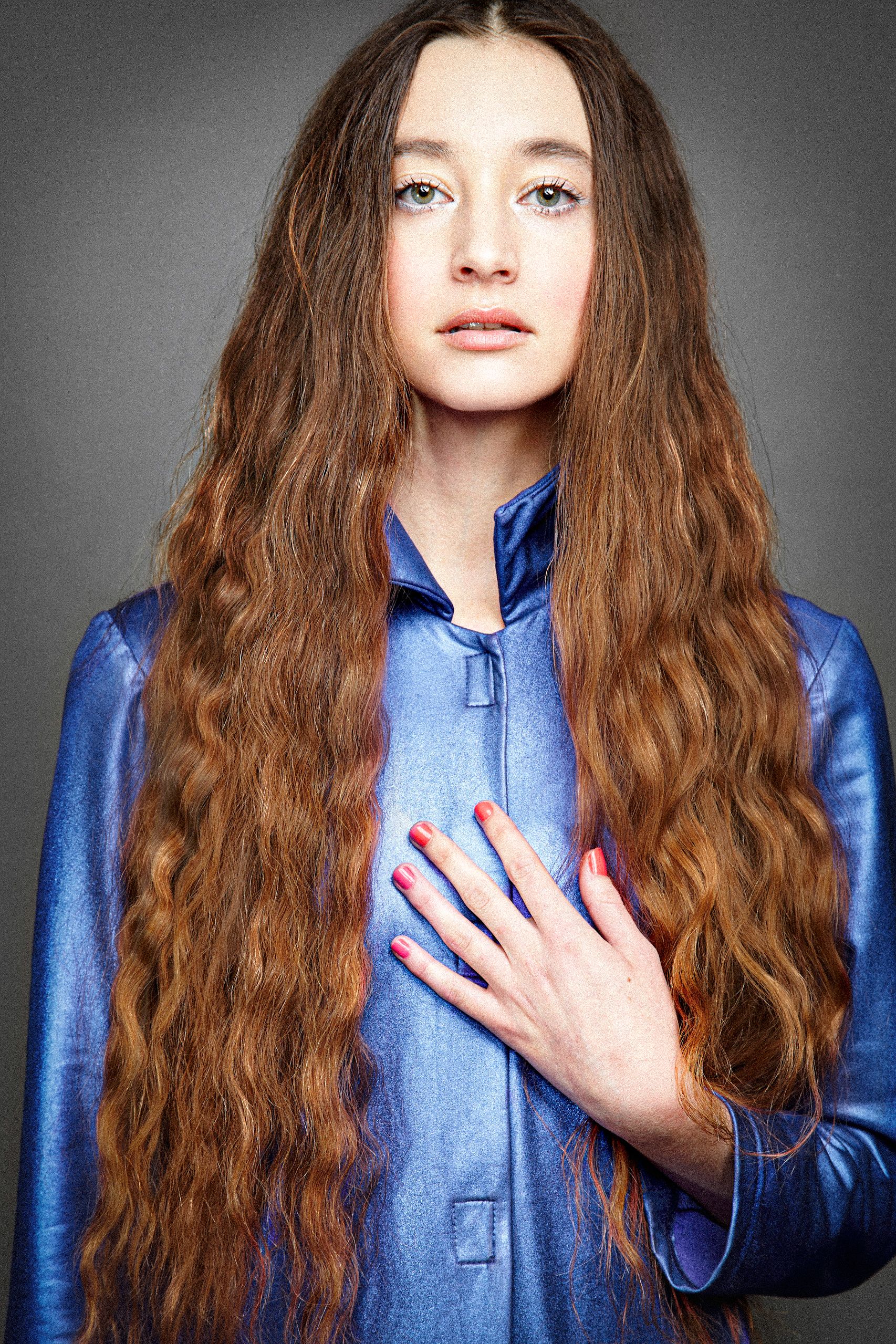 A series of portraits showing someone with long wavy brown hair wearing a bright blue silk jacket against a gray background.