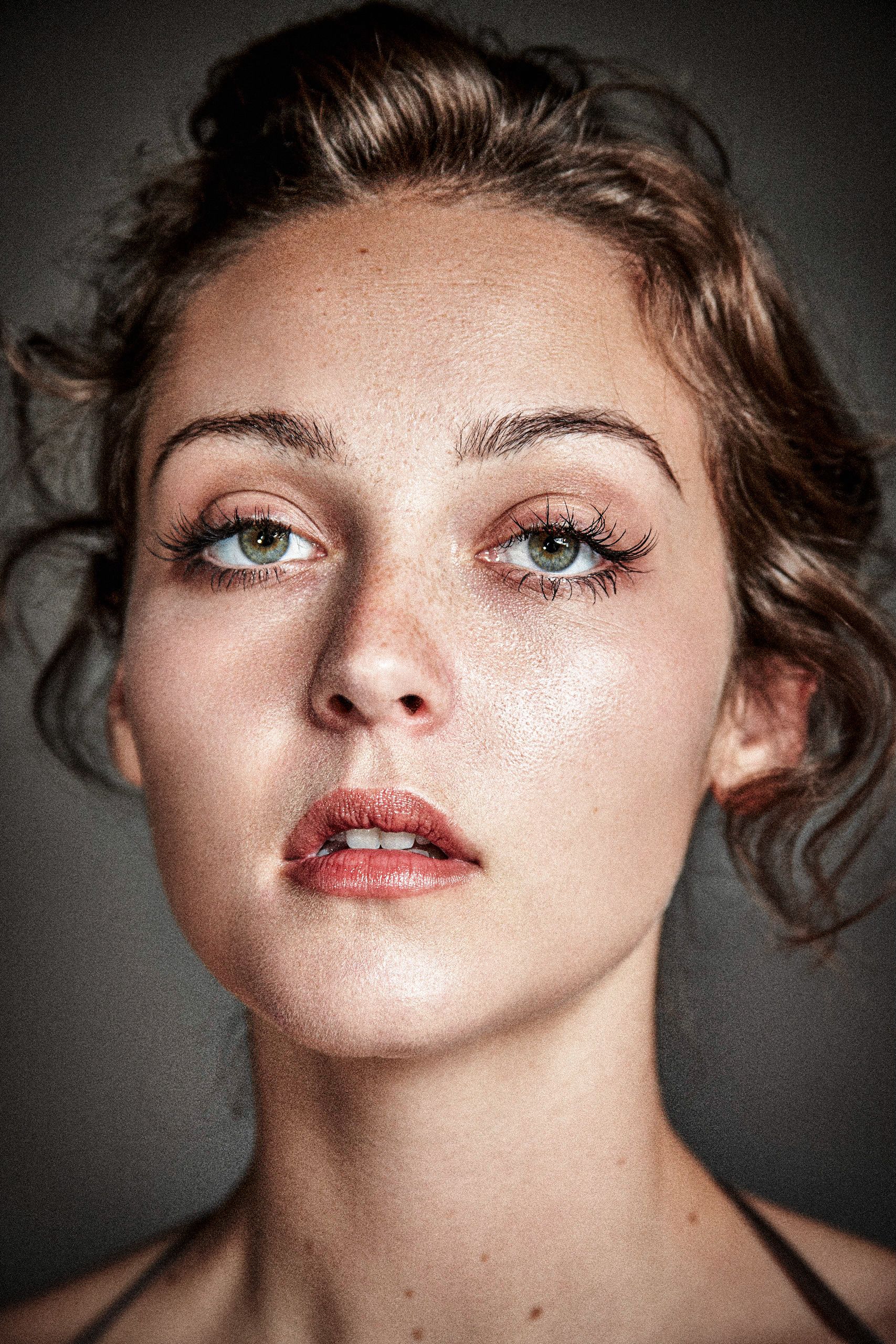 Close-up beauty portrait with dramatic lighting showcasing glowing skin, coral lipstick and styled updo against dark background.