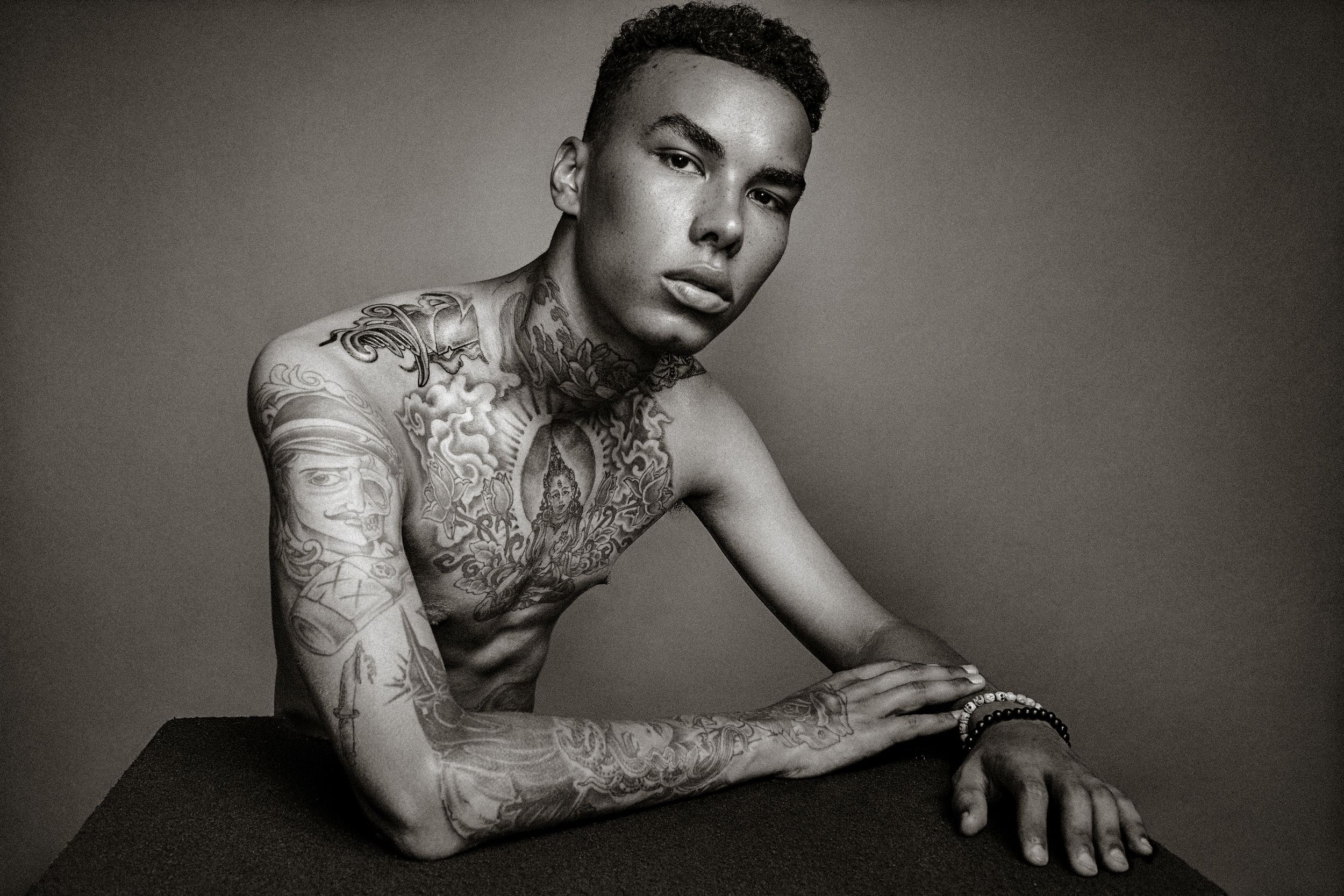 Black and white artistic portrait series showing tattooed figure in dramatic poses against dark background.