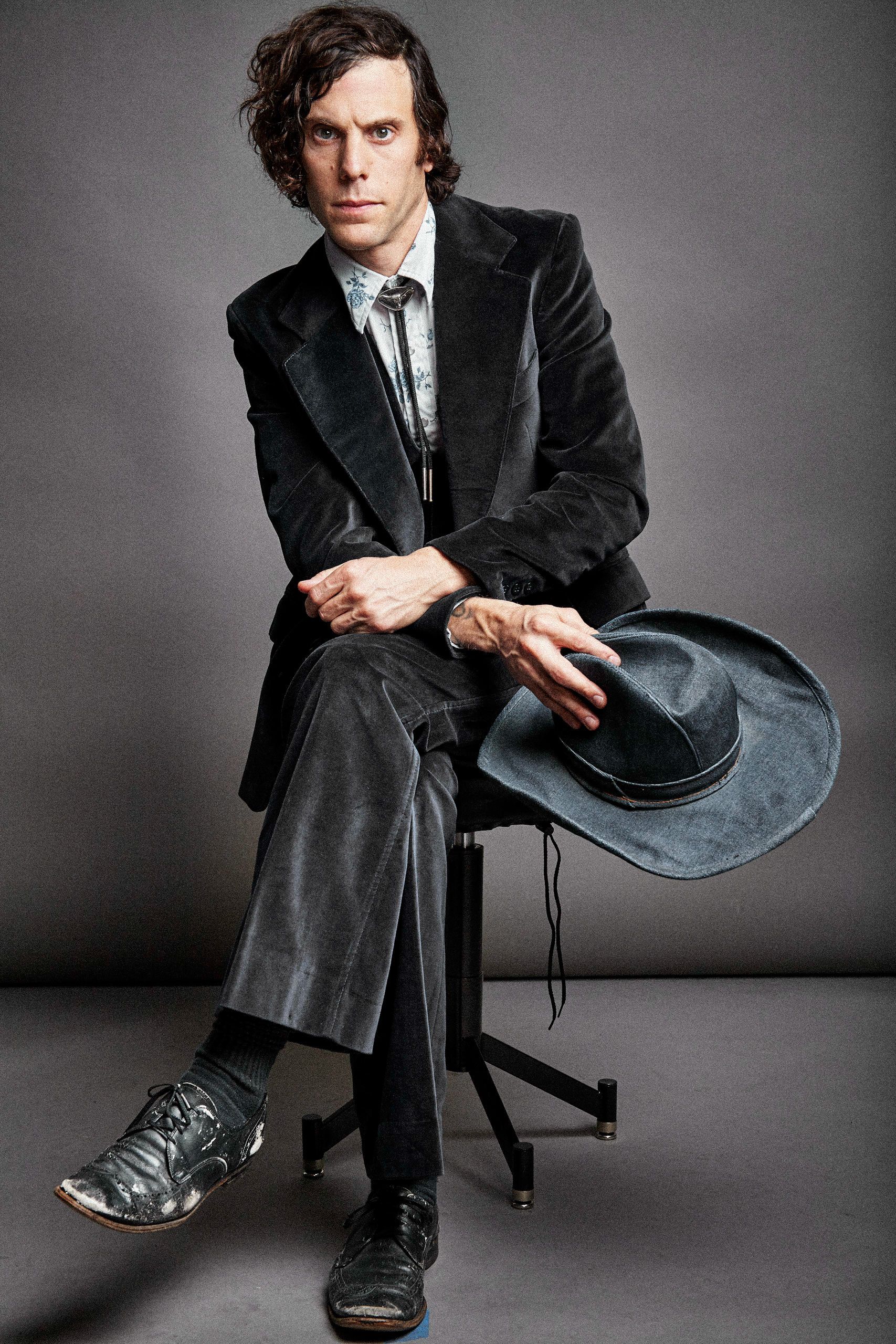 Dramatic black and white portrait series showing a person in dark suit seated on chair against gray backdrop.