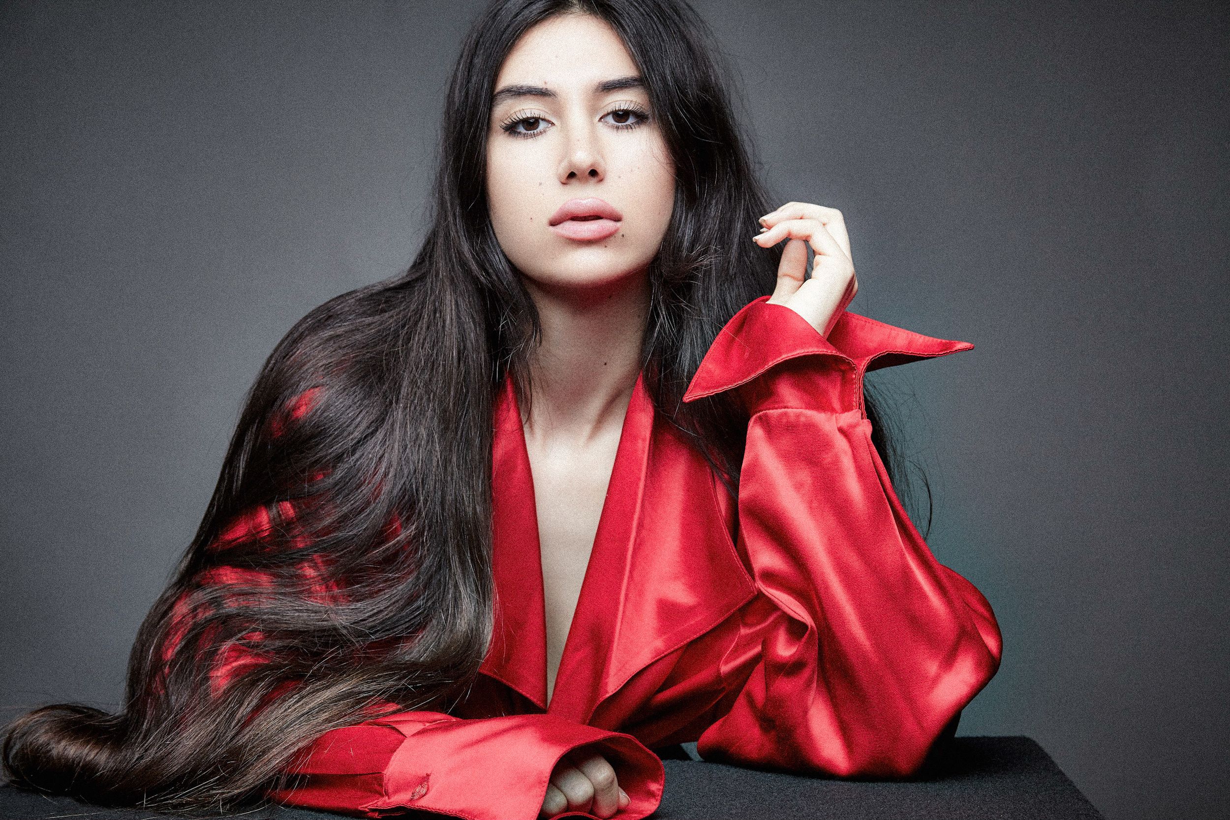 A model in a red satin blazer poses against a dark background in a glamorous fashion photoshoot.