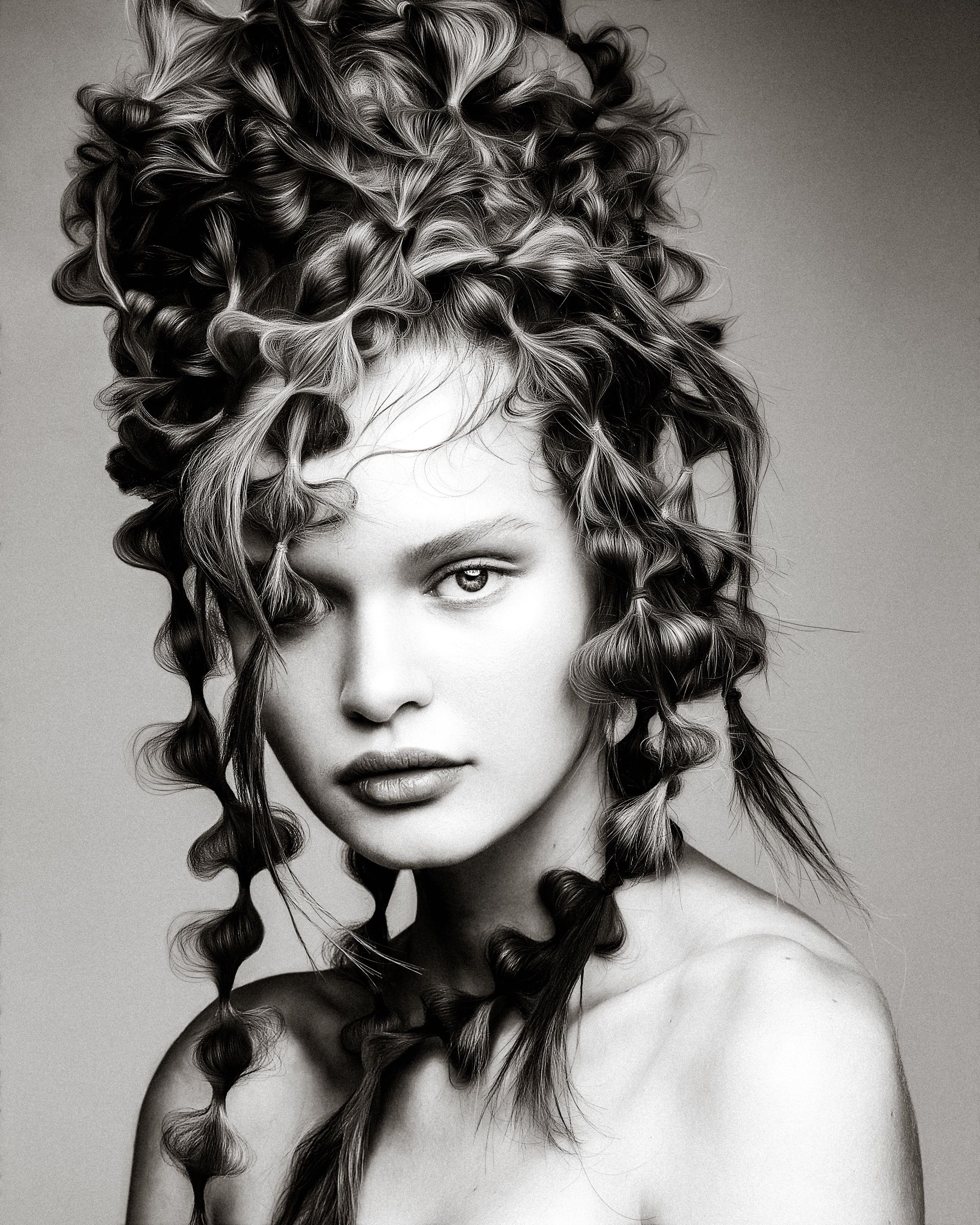 Black and white fashion portrait featuring dramatic curly hair styling with dynamic shadows and contrast.