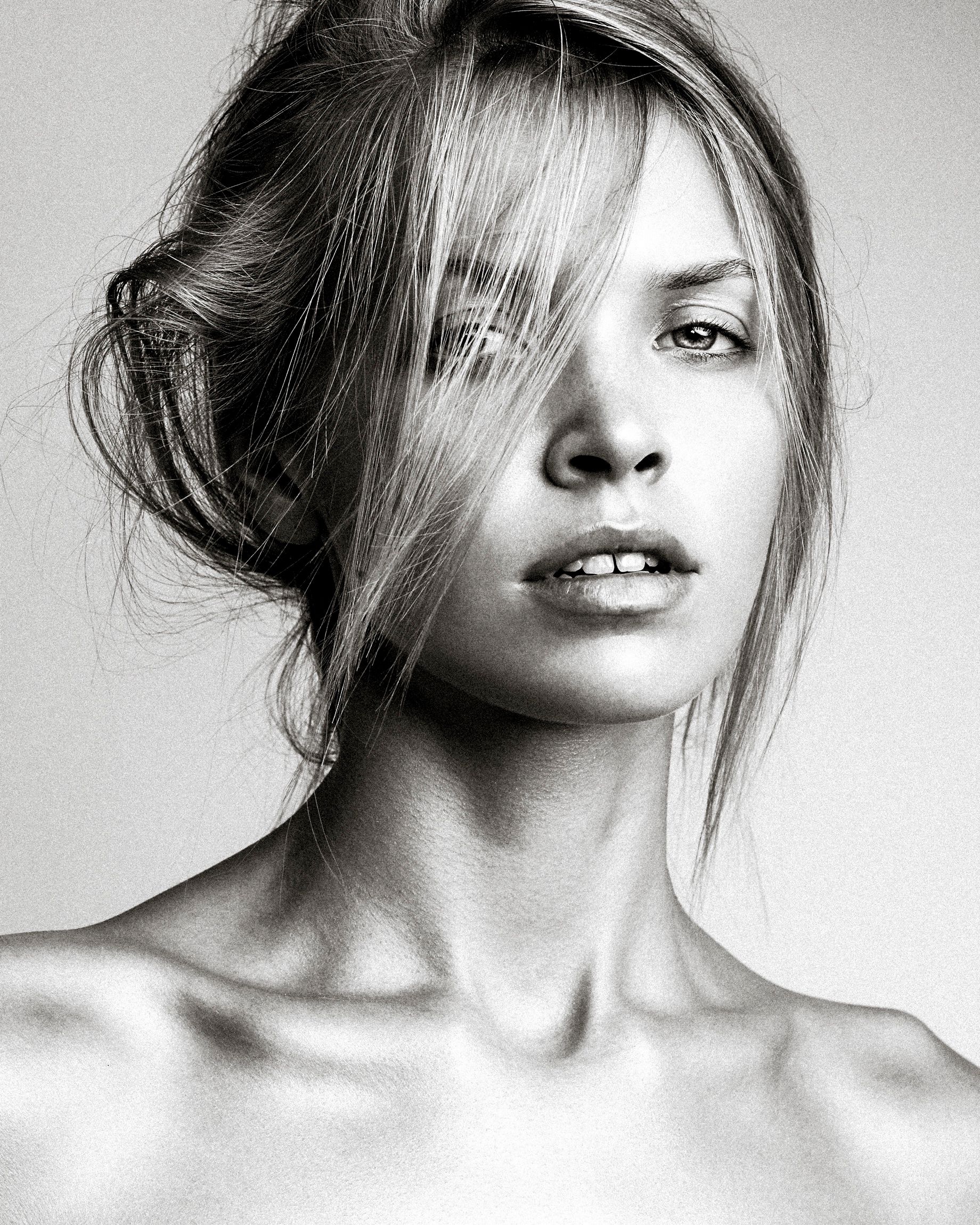 Black and white artistic portrait featuring tousled hair and bare shoulders against a light background.