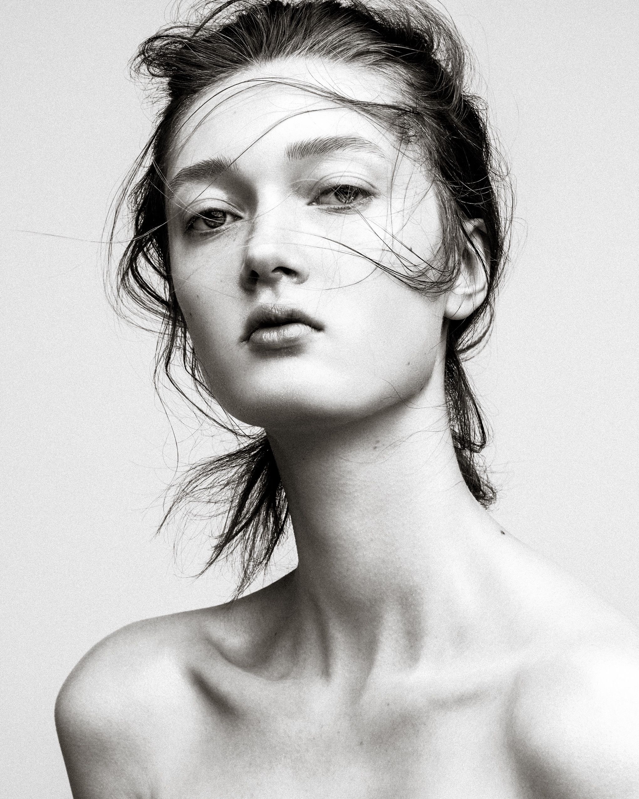 Black and white fashion portrait with windswept hair and dramatic lighting against white background.