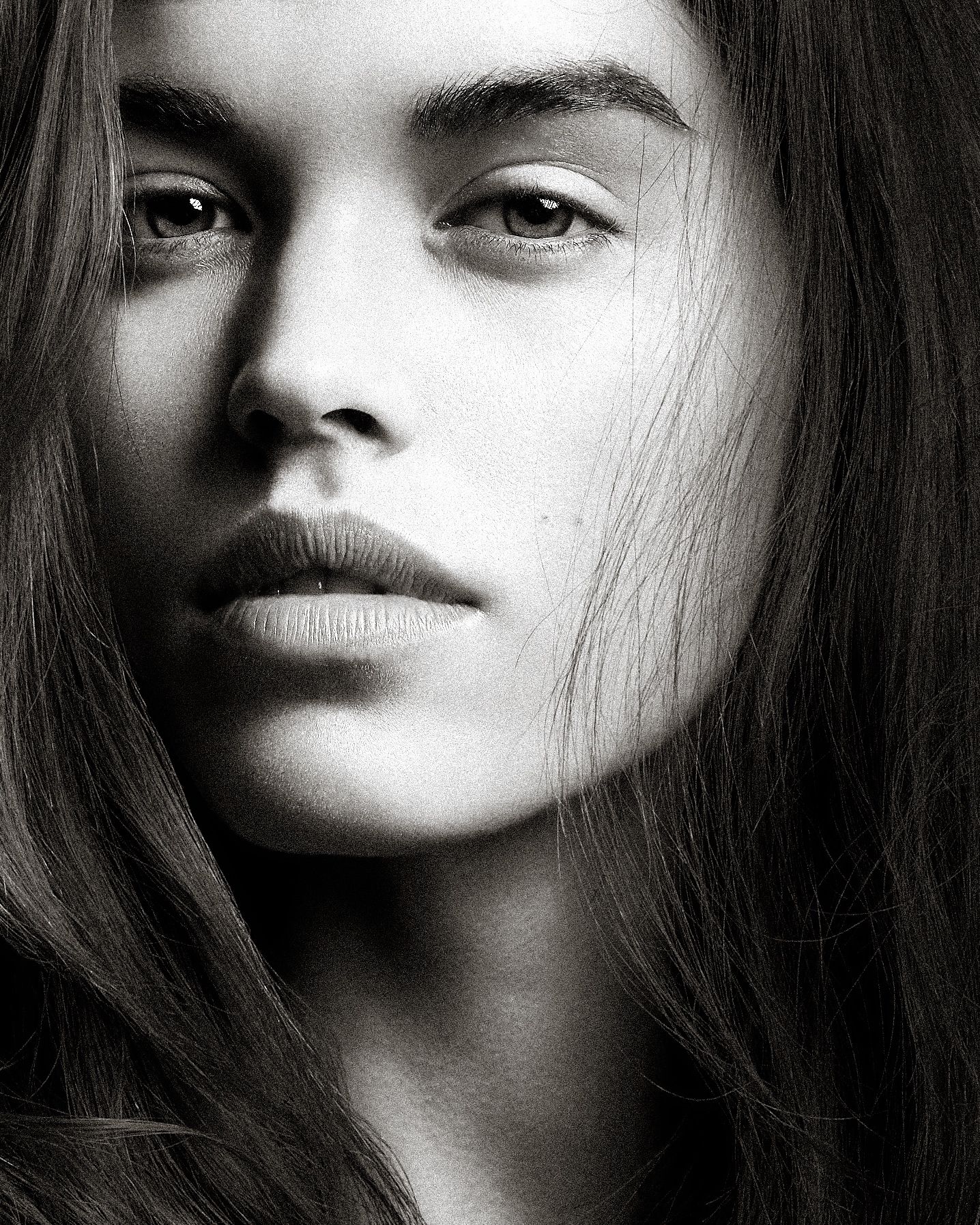 Dramatic black and white close-up portrait featuring long dark hair and striking facial features in moody lighting.