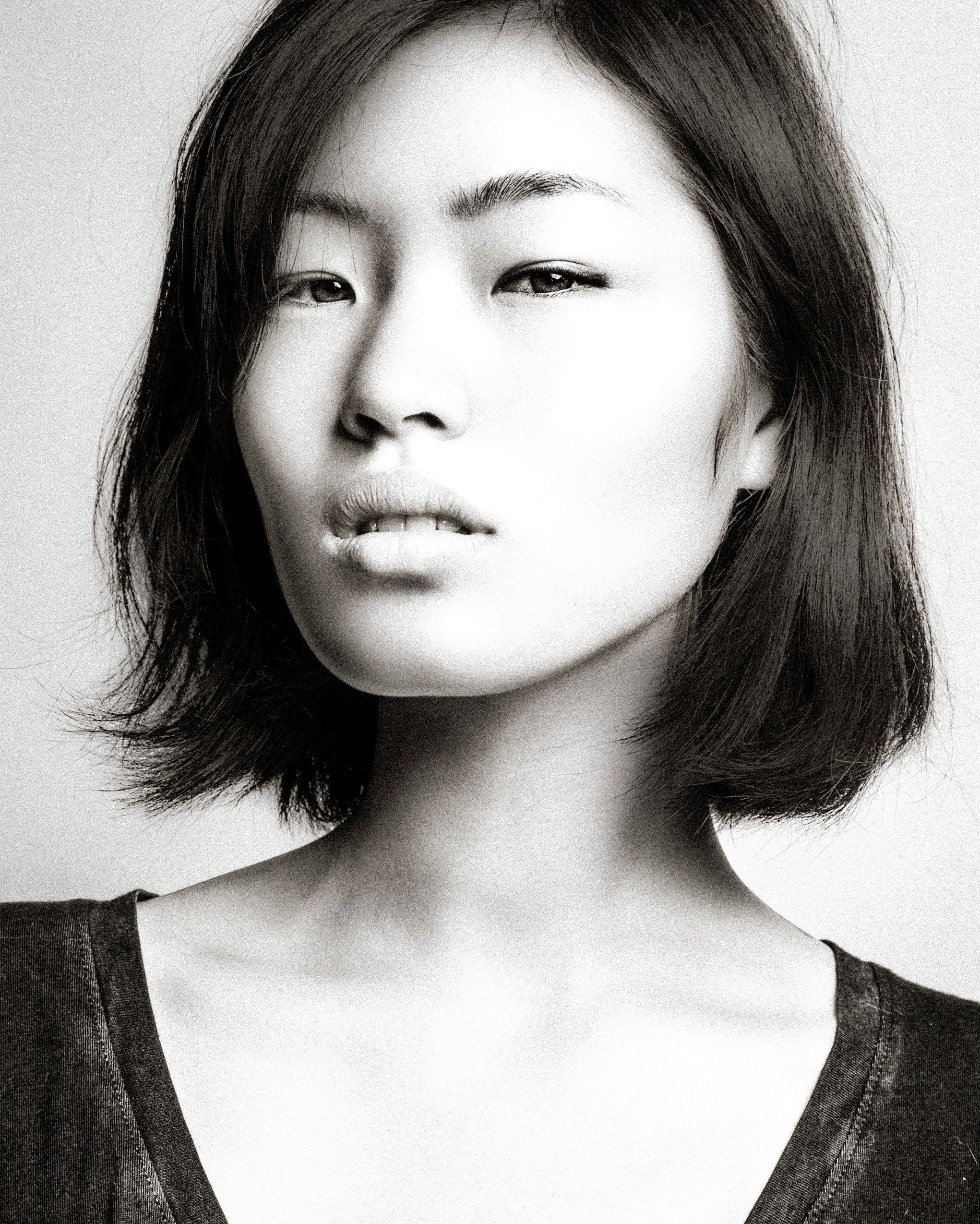 Black and white portrait photo showing a woman with shoulder-length dark hair wearing a dark top against light background.