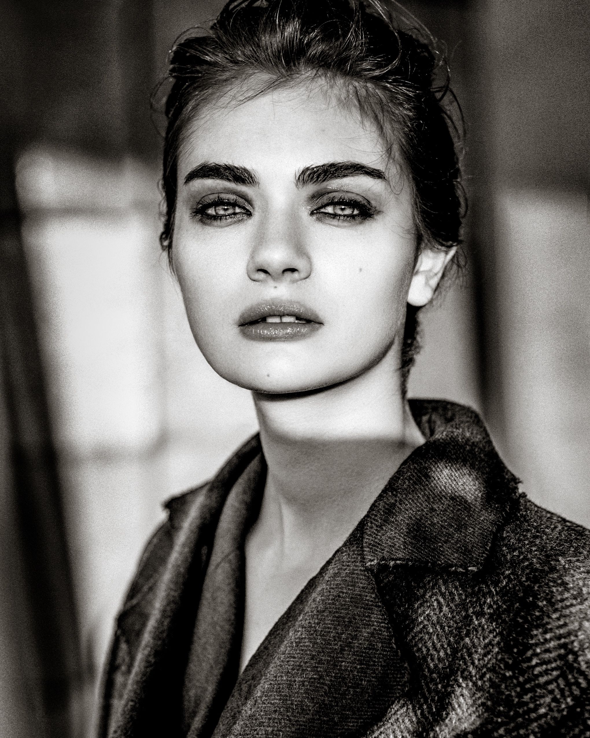 Dramatic black and white portrait of someone wearing a dark textured coat with moody lighting and artistic composition.