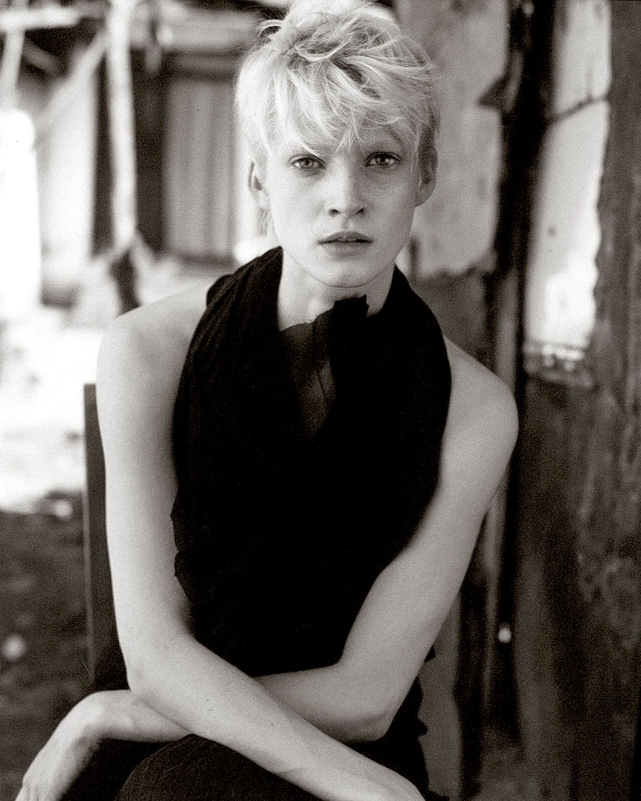 A series of four black and white portrait photos showing someone in a sleeveless black top against a blurred background.