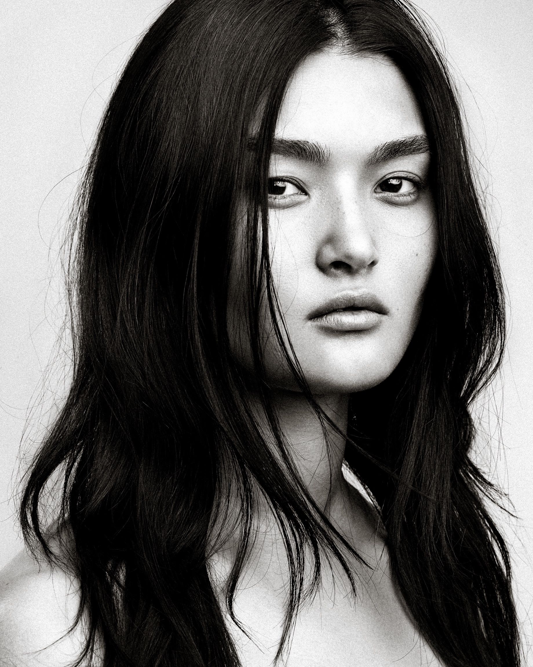 Black and white portrait photograph showing long dark hair and striking features against a light background.