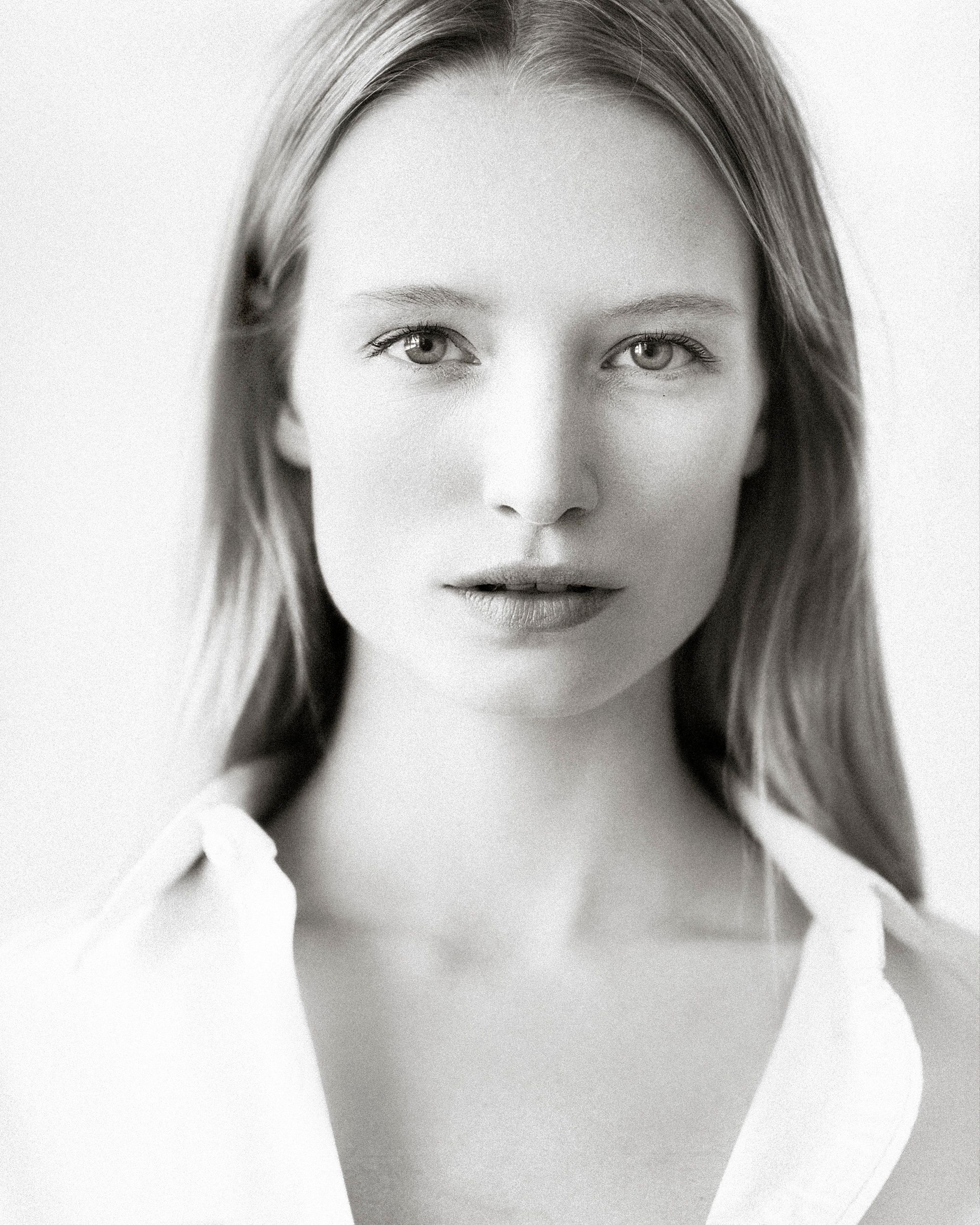 Black and white portrait photograph showing a person with straight blonde hair wearing a white collared top.