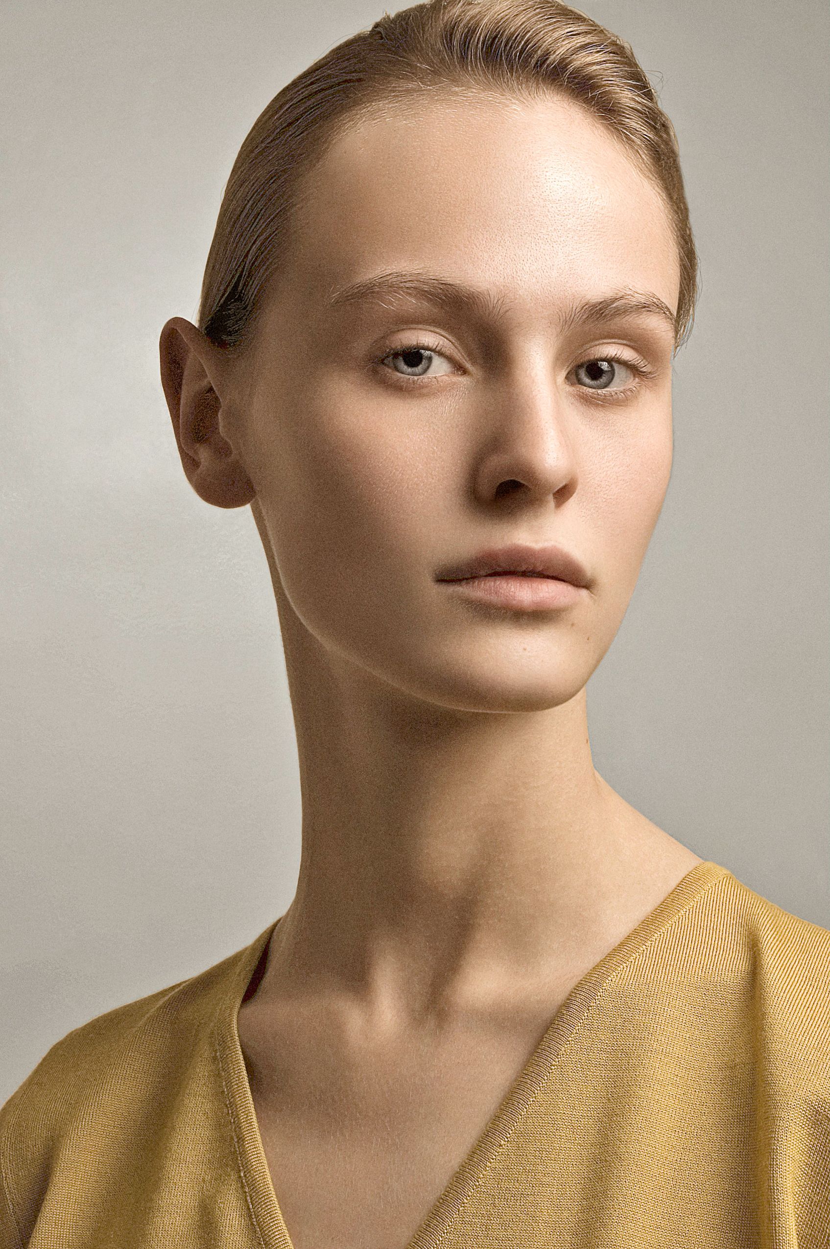 Professional portrait in warm tones featuring a person in a mustard yellow top against a neutral background.