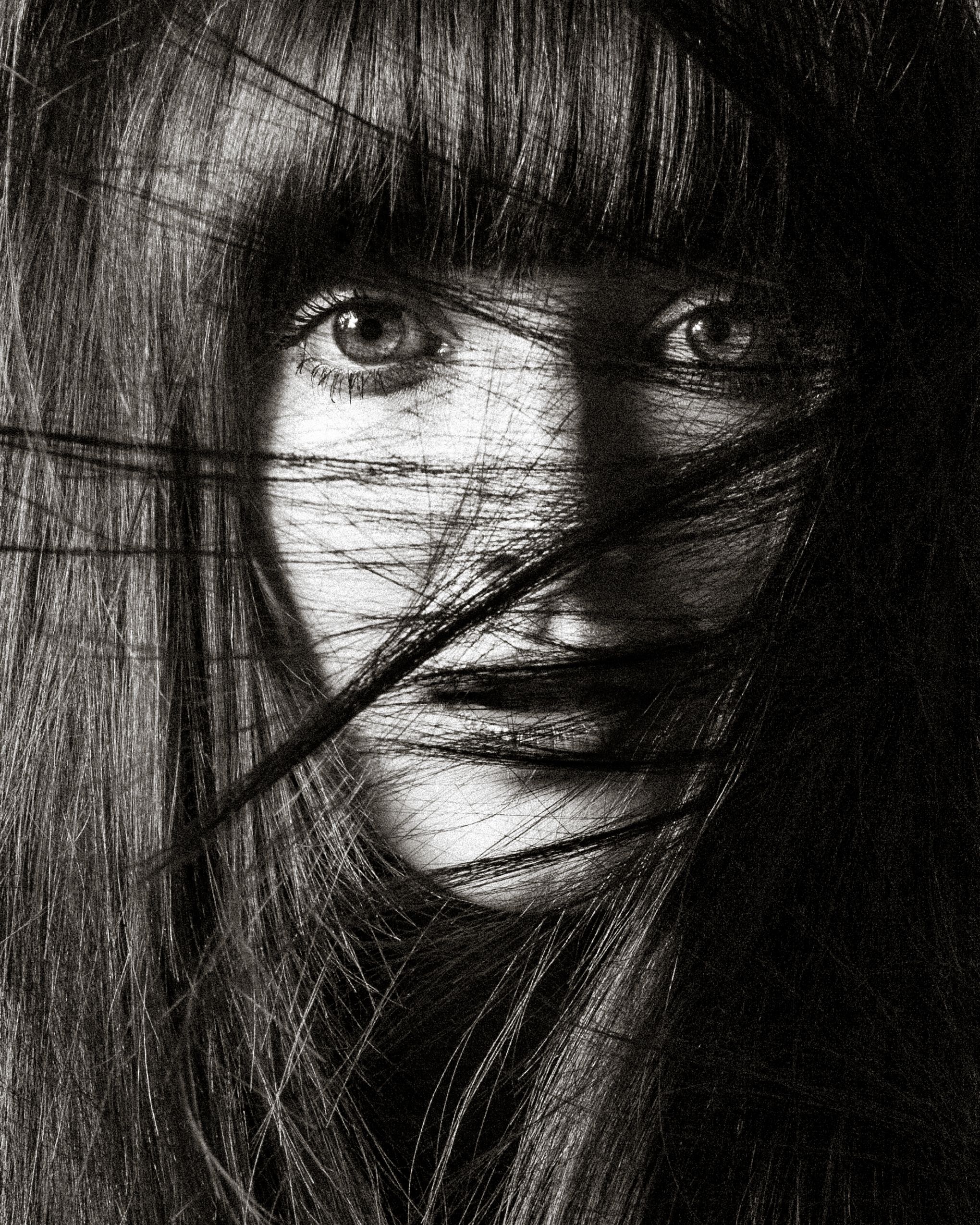 Black and white artistic portrait showing dark hair partially obscuring eyes in dramatic shadow and contrast.