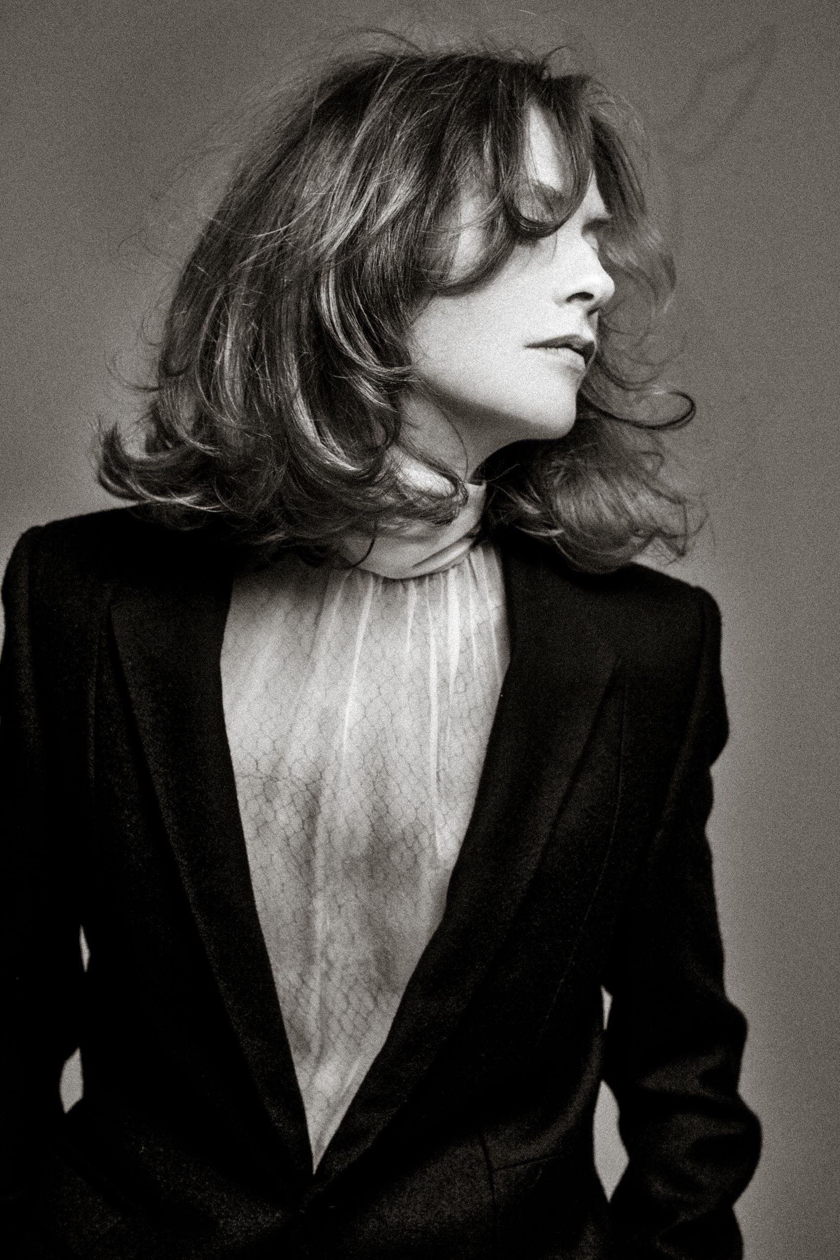Black and white portrait of a person in a dark blazer with flowing hair, looking to the side in dramatic lighting.