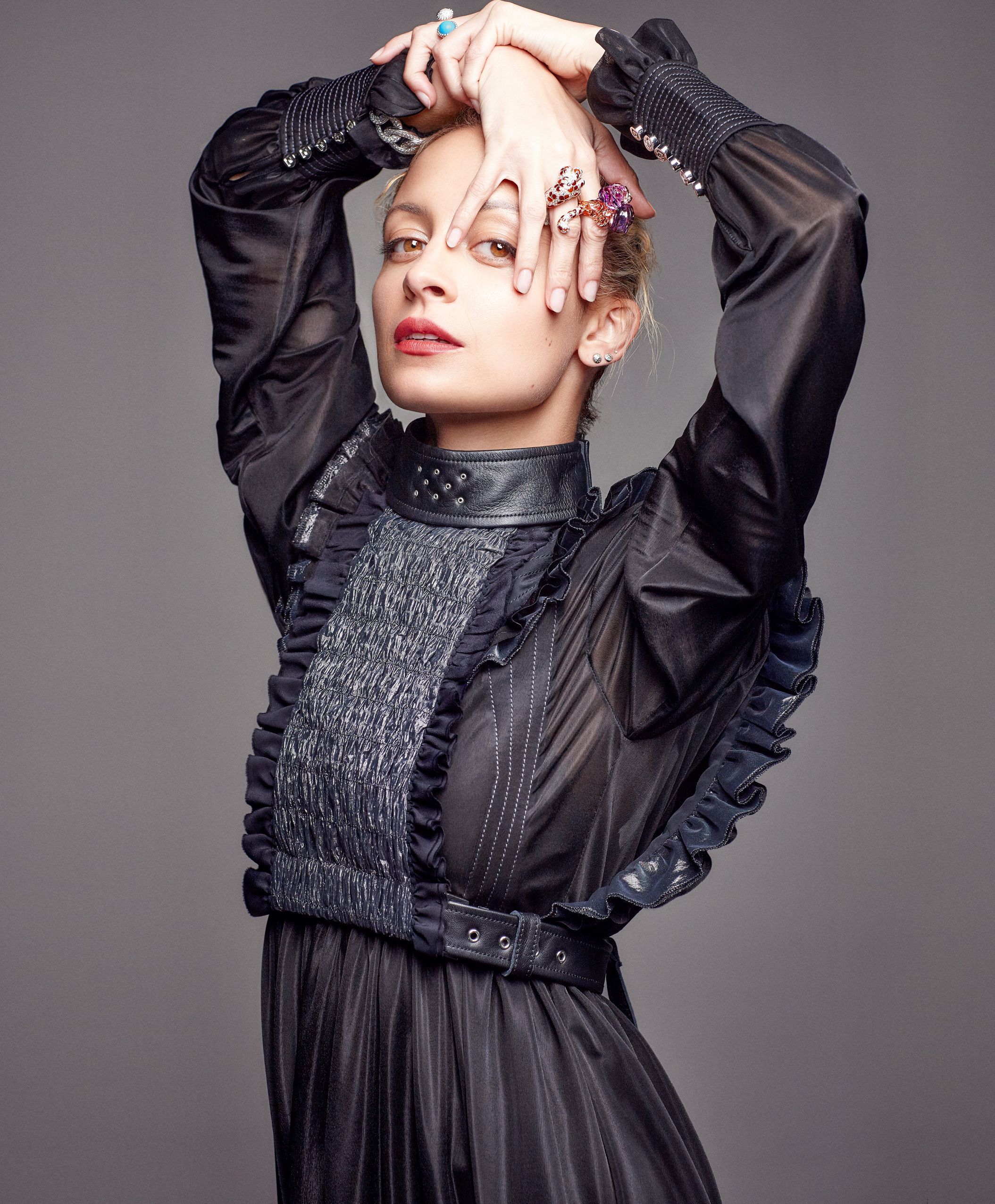 Fashion model in dramatic black dress with smocked bodice and ruffled sleeves poses against gray backdrop.