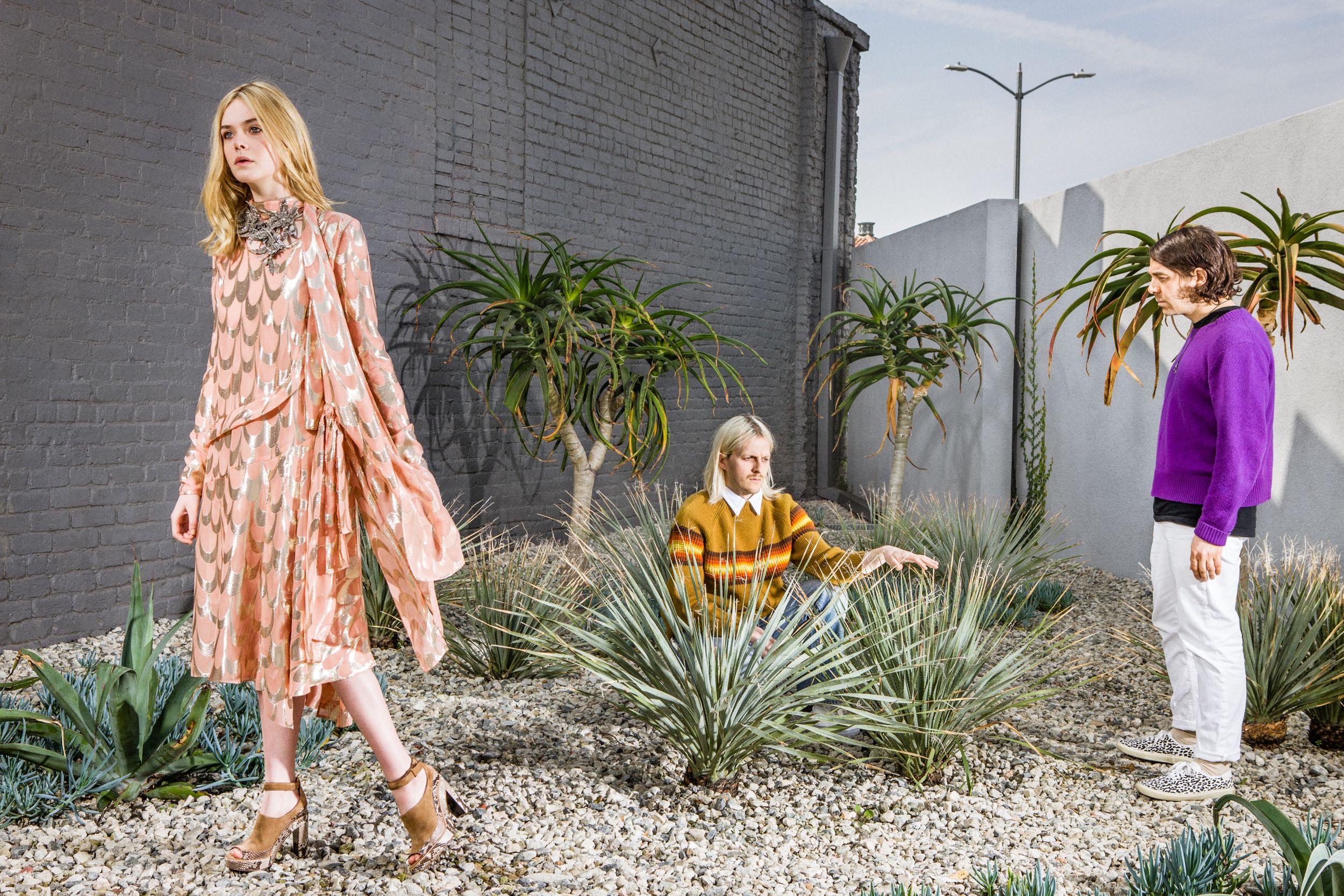 Three people pose in colorful spring outfits against a modern landscaped backdrop with desert plants and palm trees.