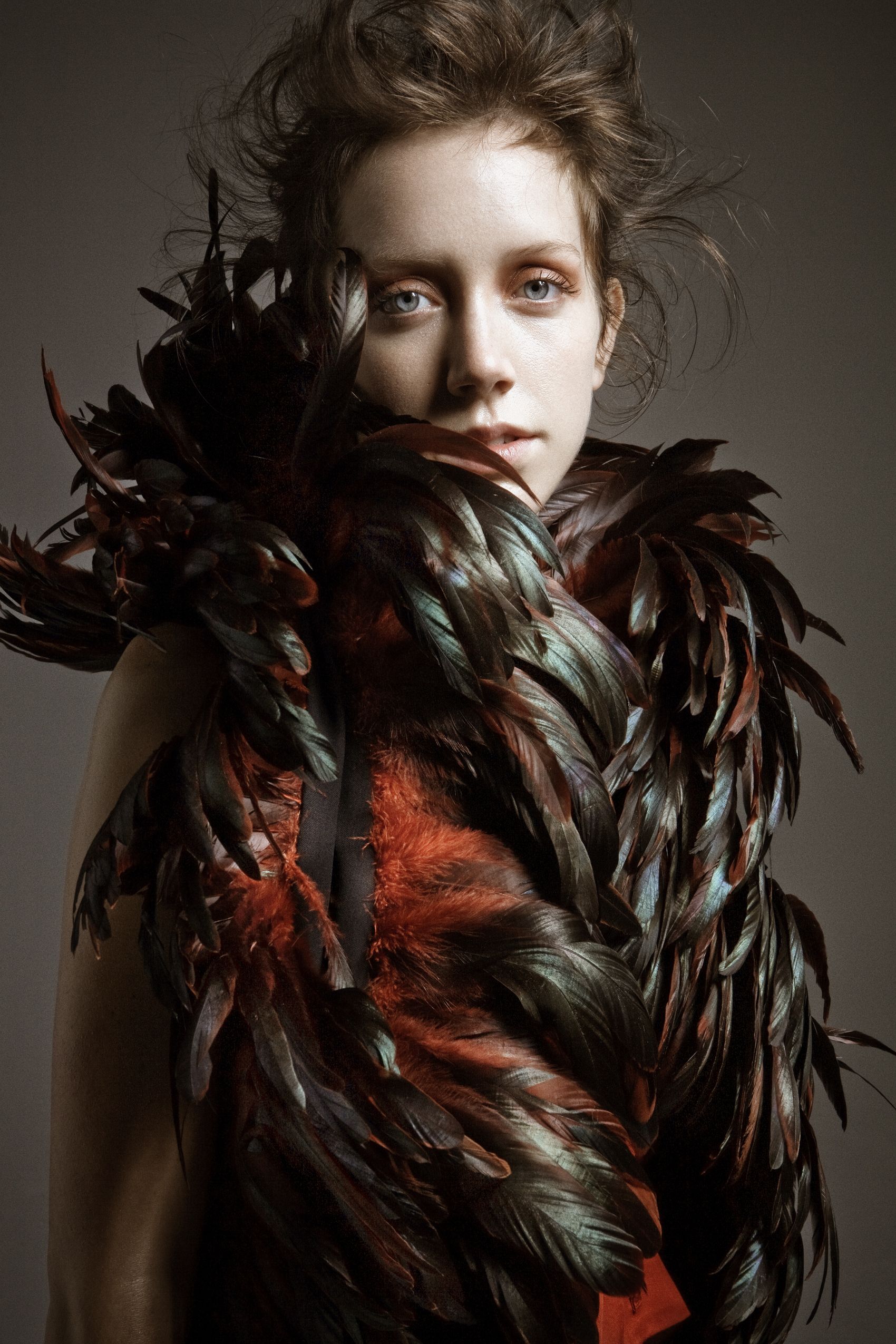 Dramatic fashion portrait series featuring dark feathers and moody lighting against a studio backdrop.