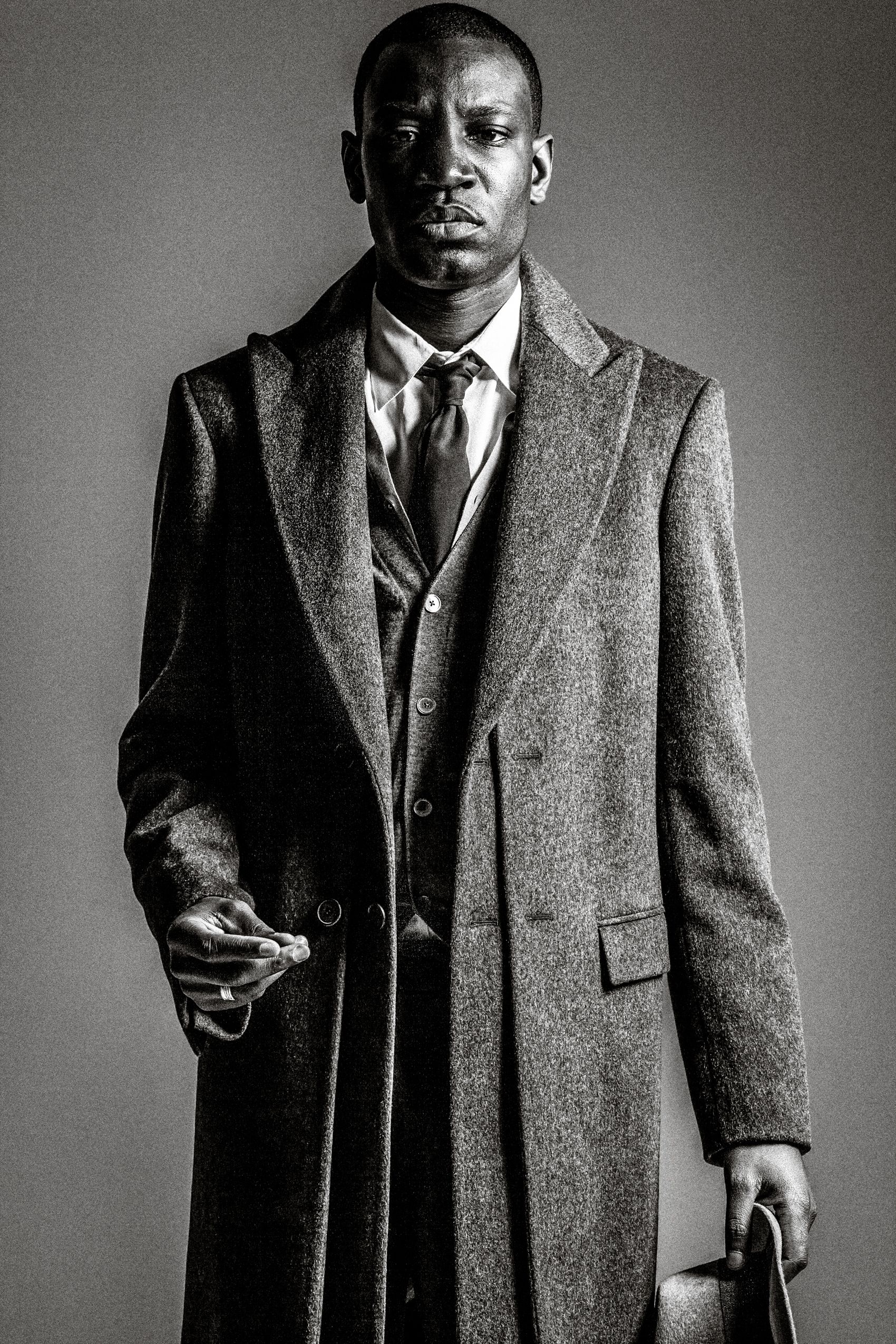 A series of black and white photos showing a person in a tweed overcoat and suit standing in different poses.